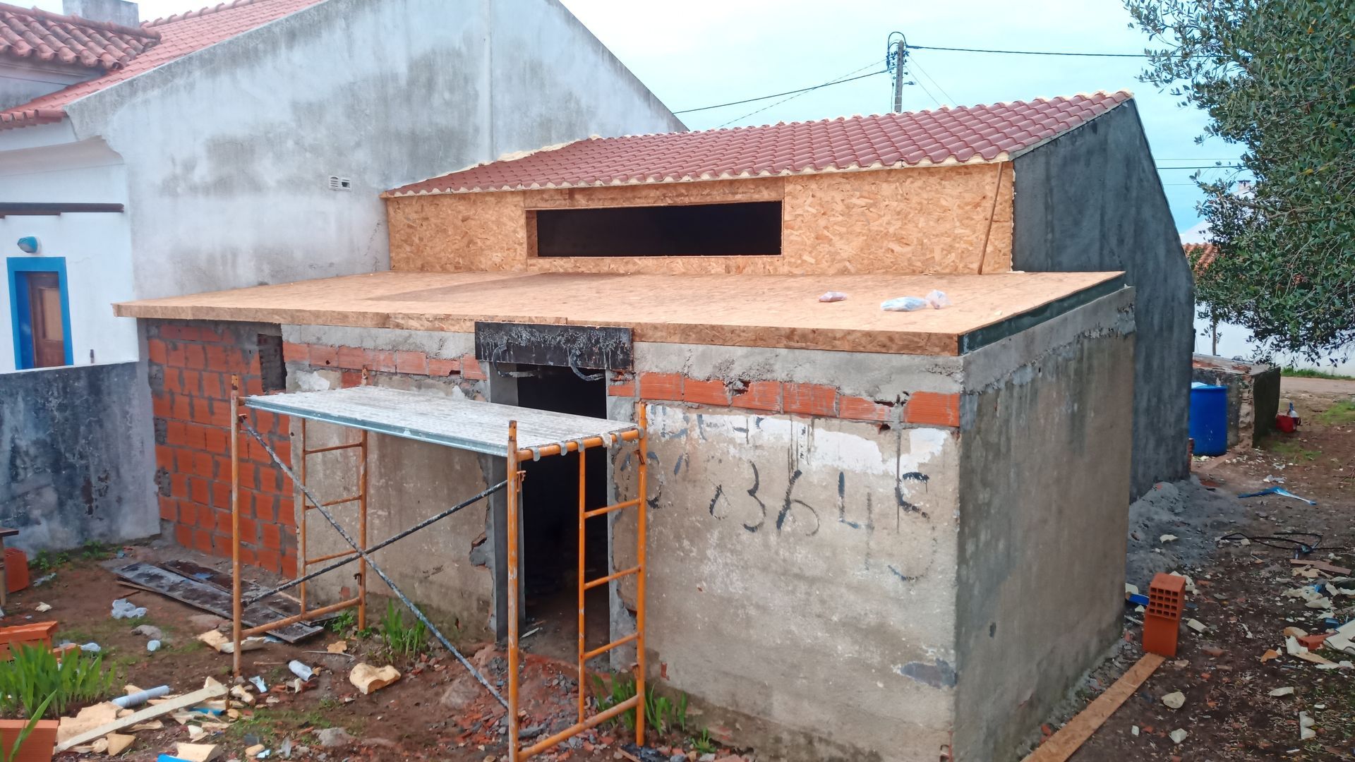 Construção de um pequeno edifício de concreto; tijolos vermelhos, madeira e telhado de telhas são visíveis.