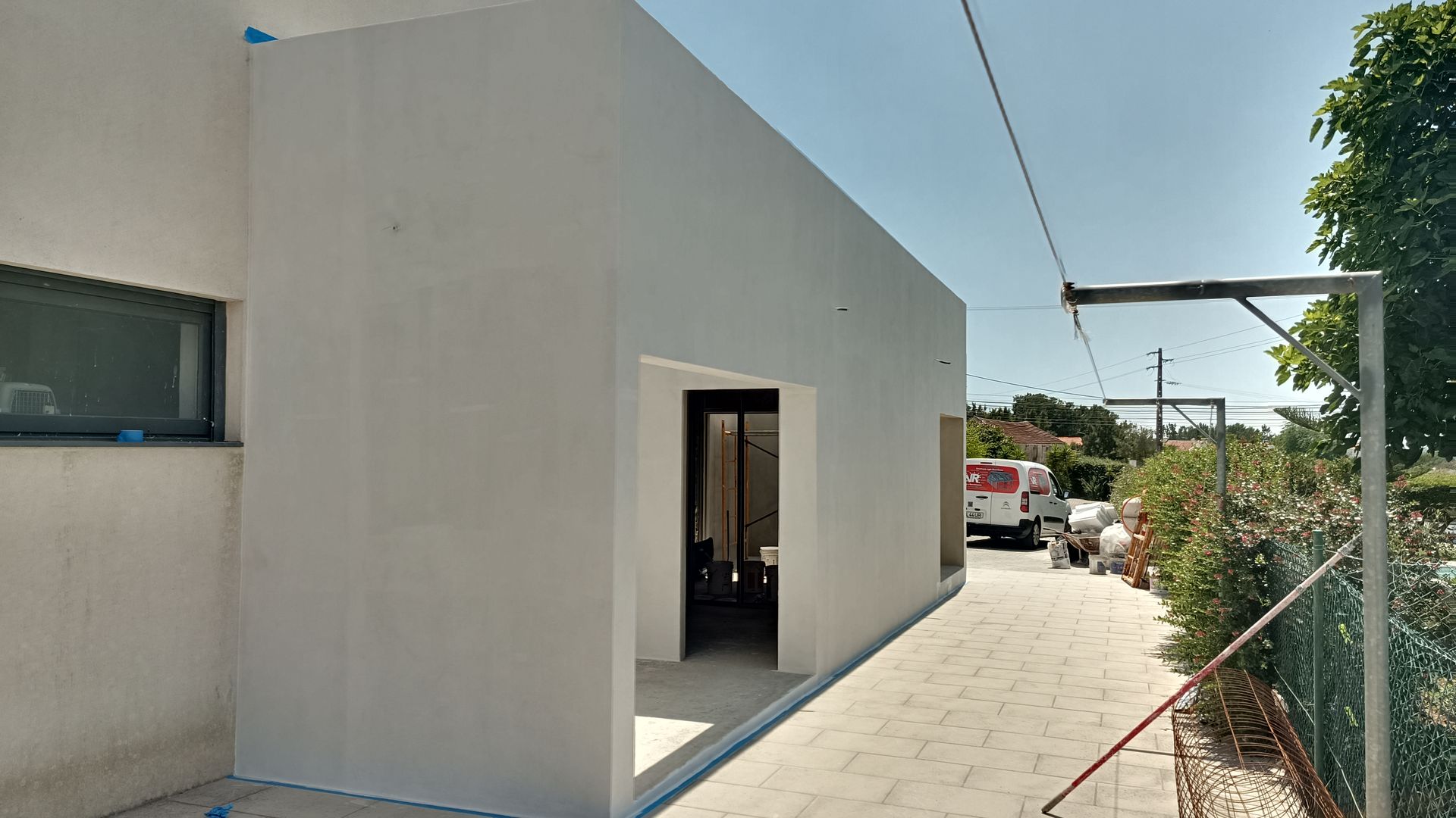 Exterior de um edifício em construção, pintado de branco, com uma porta aberta que dá acesso a um espaço interior.