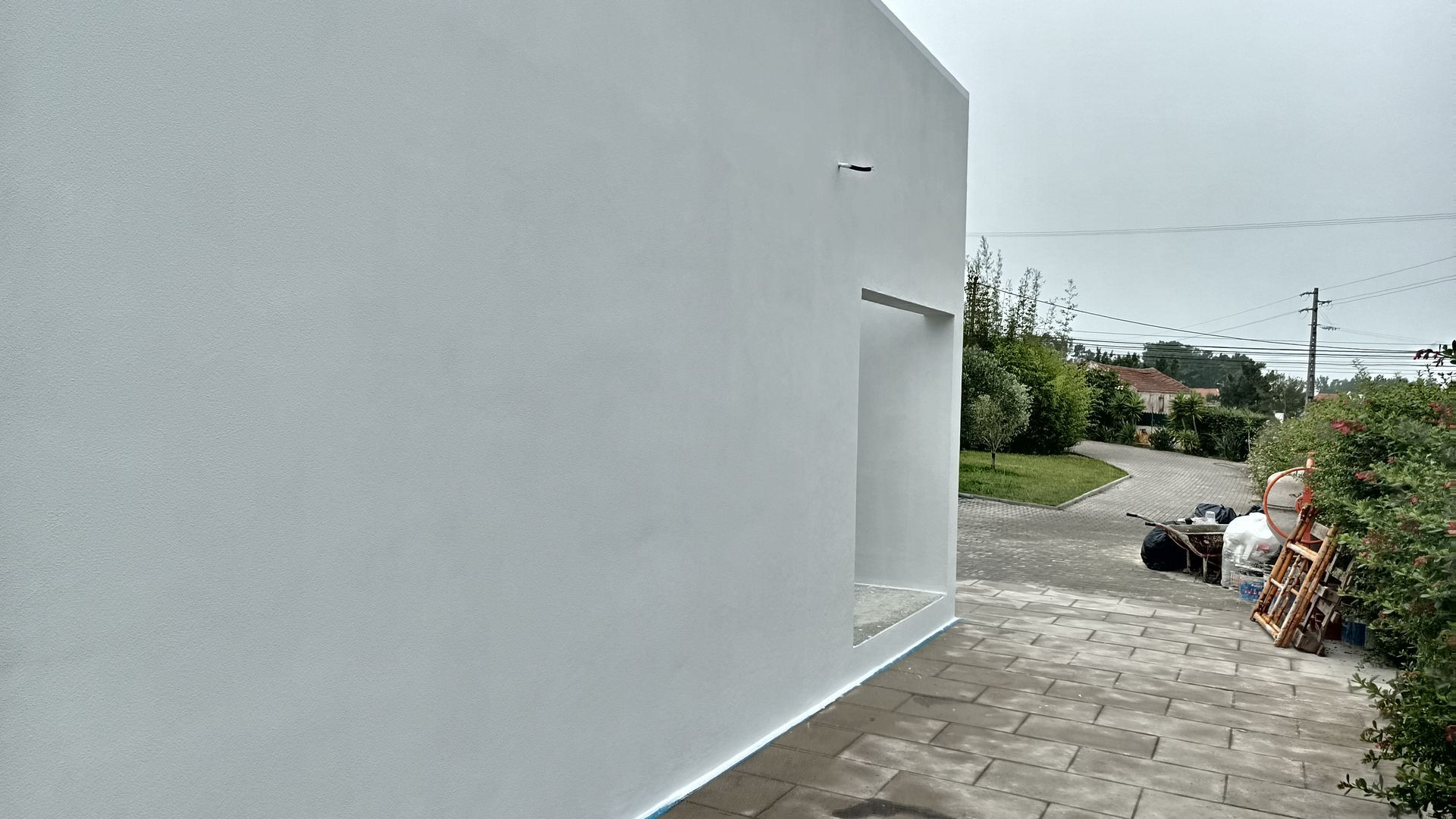 Prédio branco com porta recuada, vista externa. Calçada pavimentada ao lado, vegetação ao fundo.