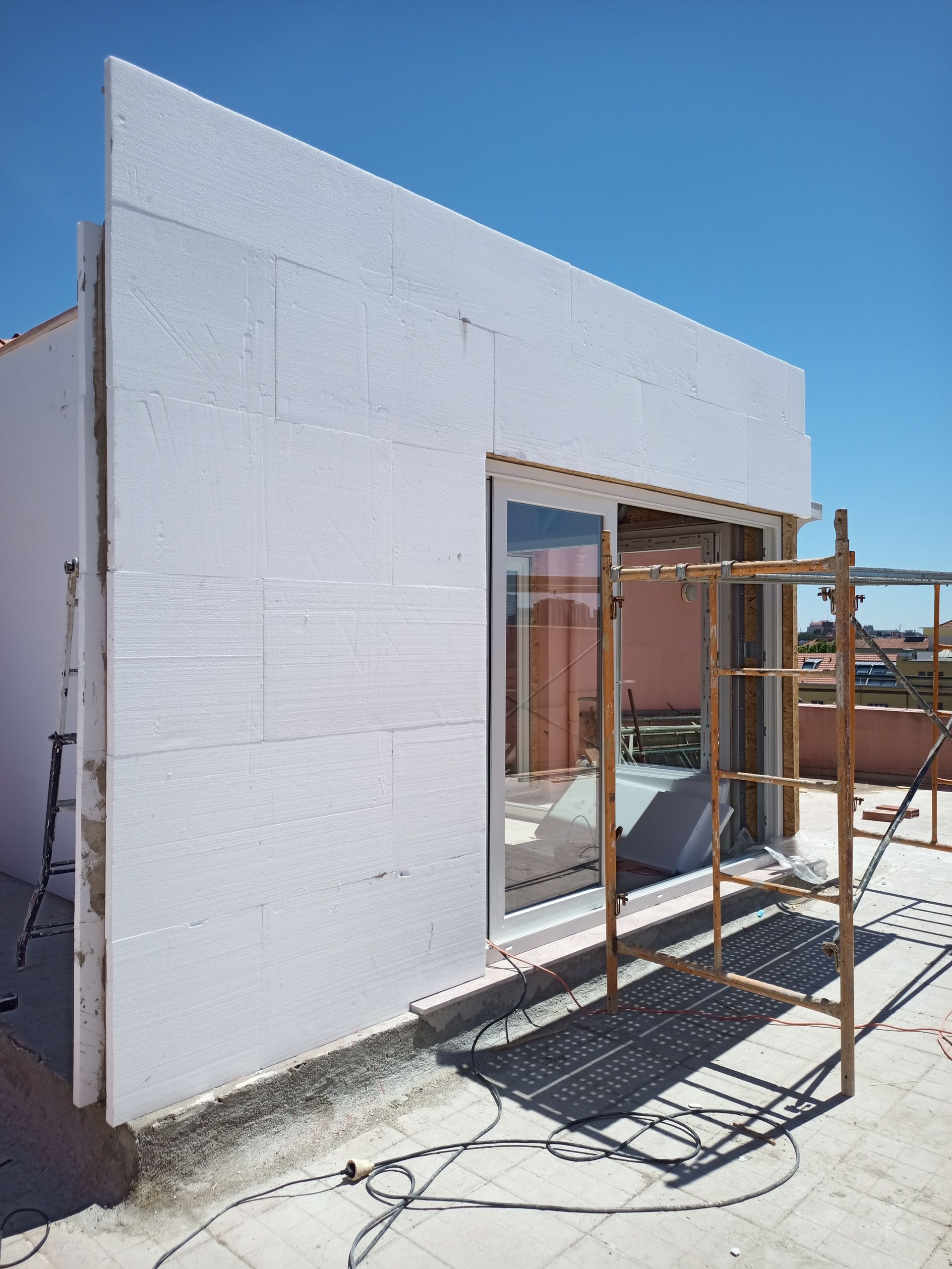 Construção da parede externa com painéis isolantes brancos, caixilho de janela e andaimes no telhado.