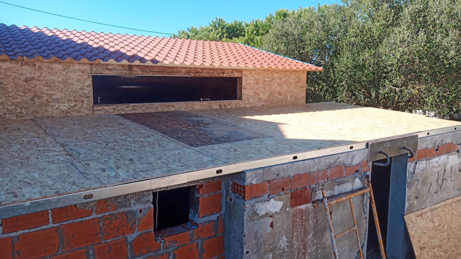 Prédio em construção com telhado de telha vermelha e revestimento em OSB.