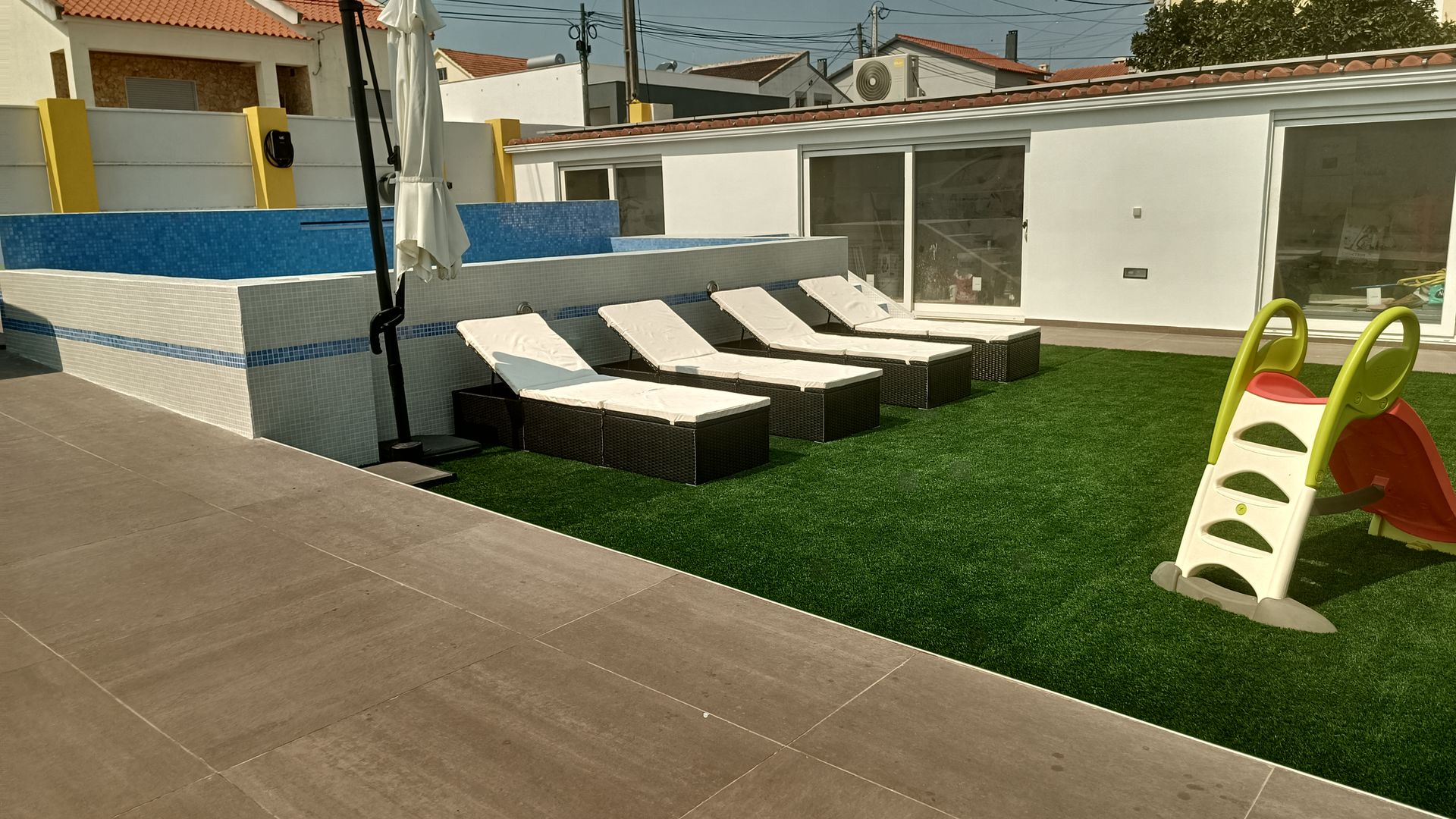 Espreguiçadeiras e um pequeno escorregador em grama artificial ao lado da piscina.
