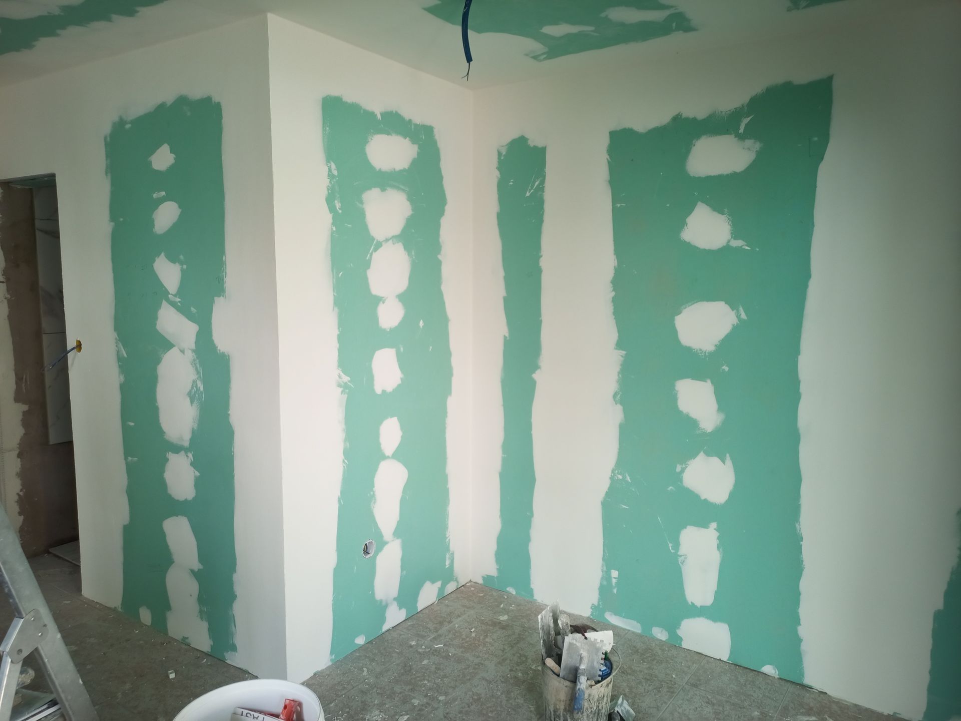 Canto interno com drywall parcialmente instalado, mostrando superfícies verdes e brancas expostas.