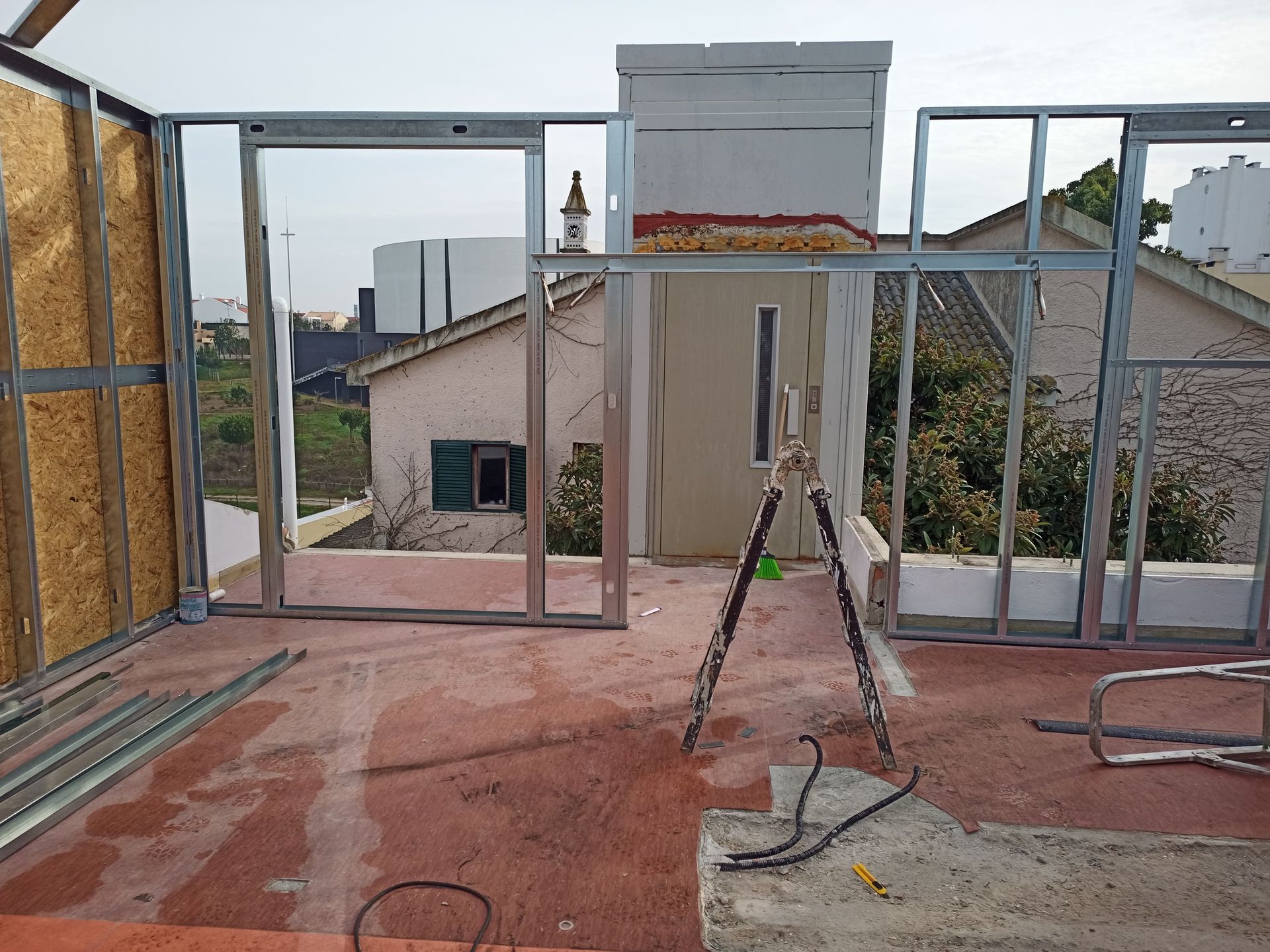 Construção de uma sala com estrutura metálica em um terraço. A estrutura se destaca contra o pano de fundo de prédios e céu.