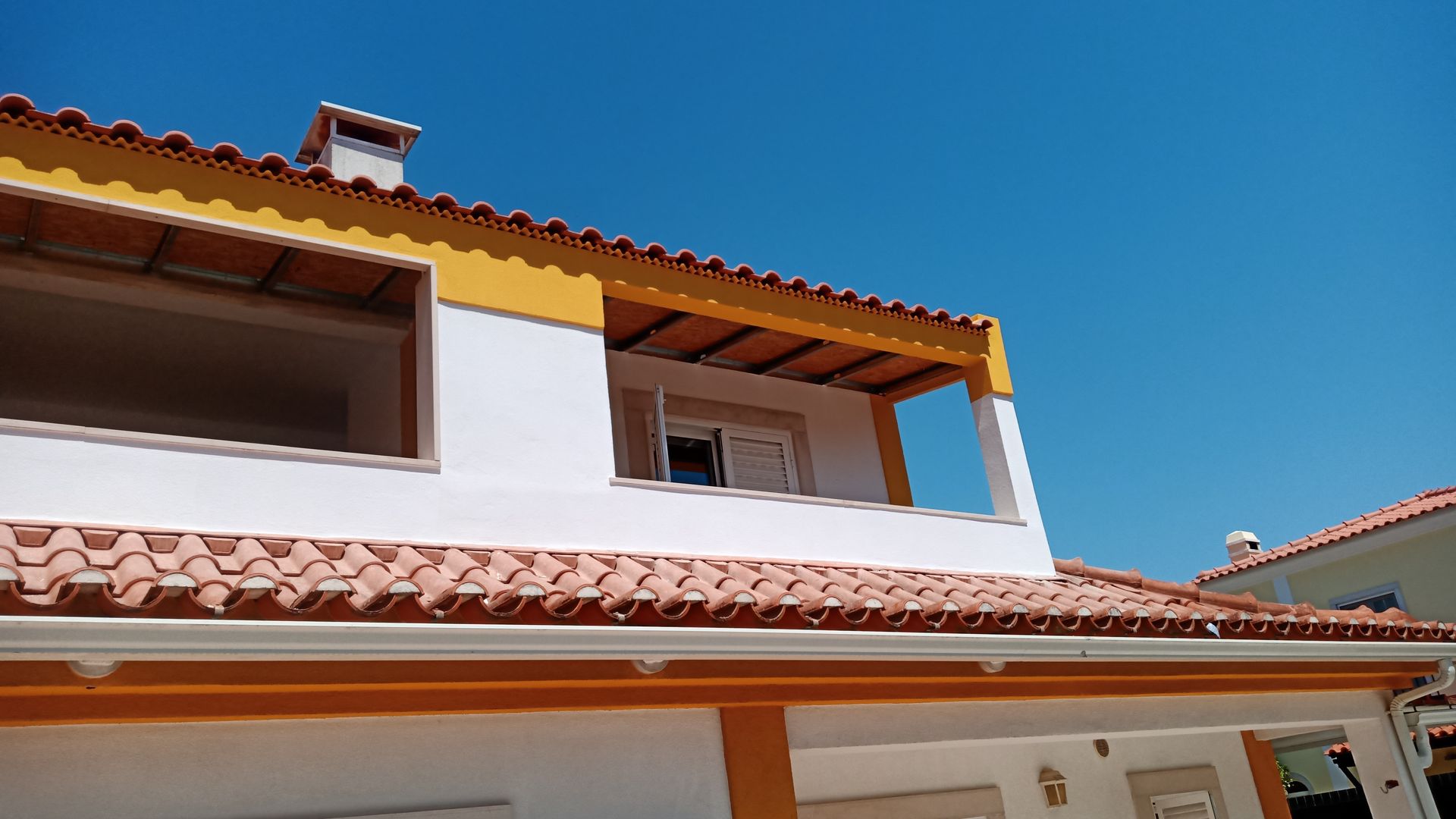Casa branca com detalhes em laranja e telhado de telha vermelha contra um céu azul brilhante.
