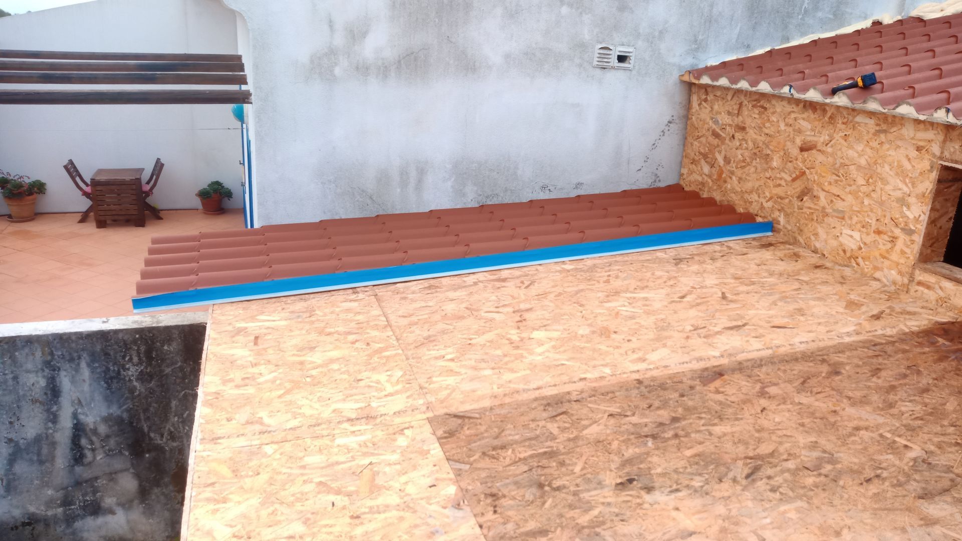 Construção do telhado: painéis OSB com uma seção de telhas vermelhas e acabamento azul.