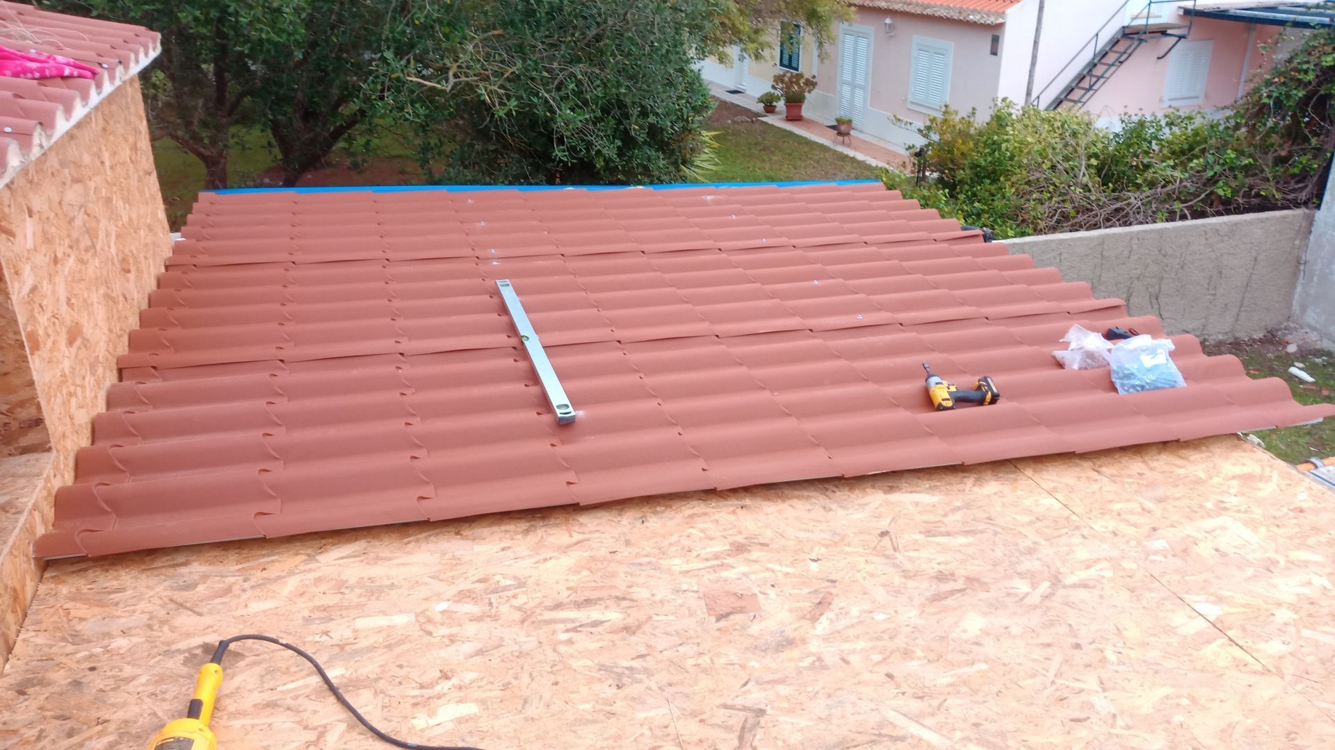 Obra de cobertura em andamento: painéis ondulados marrons colocados sobre placa OSB; ferramentas e um nível visíveis.