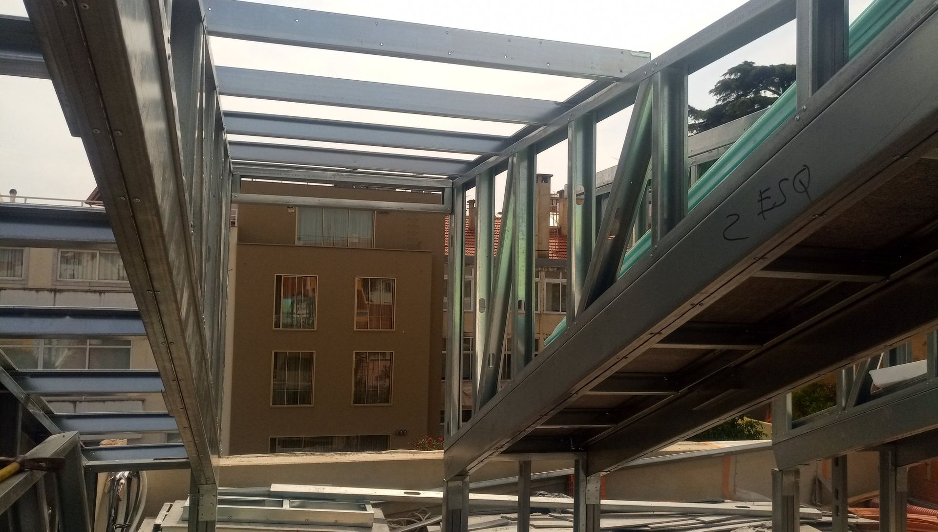 Estrutura metálica para um edifício em construção, com vigas horizontais e suportes verticais; um edifício ao fundo.
