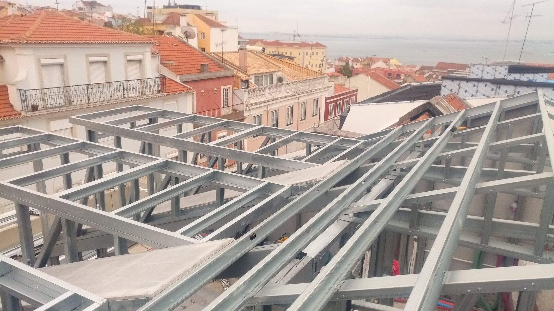 Estrutura metálica em construção em um telhado, com prédios e o oceano ao fundo.