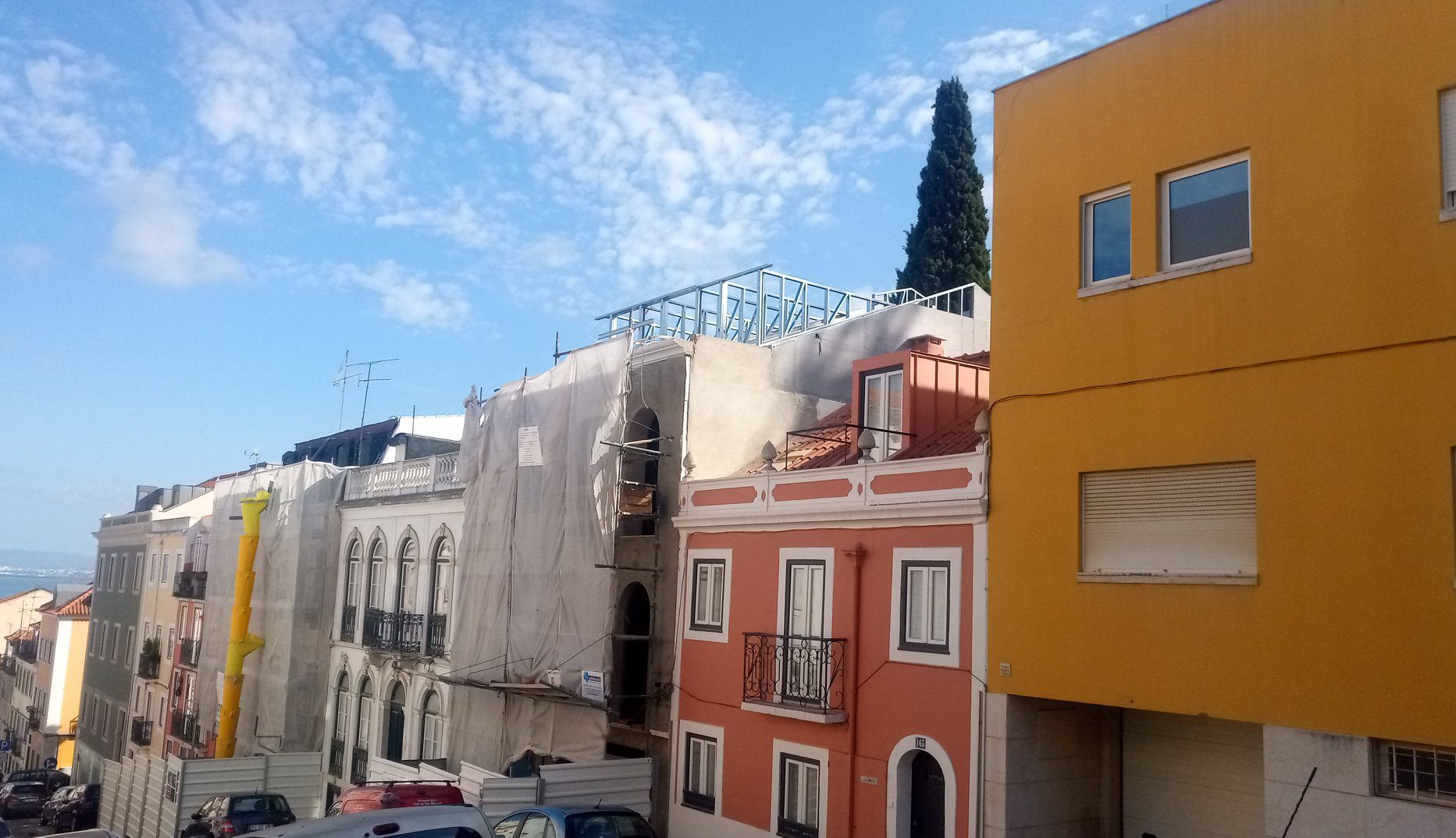Prédios coloridos alinham-se em uma rua sob um céu azul parcialmente nublado.