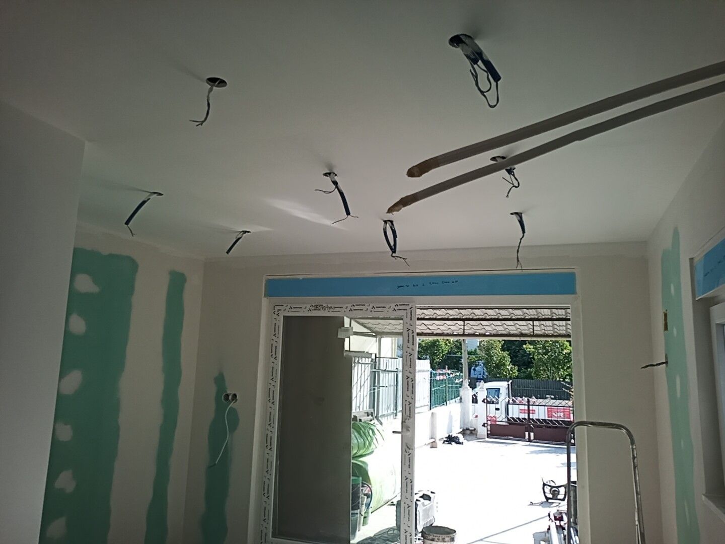 Sala interna em construção, com fiação exposta no teto. As paredes estão parcialmente revestidas com gesso acartonado verde.