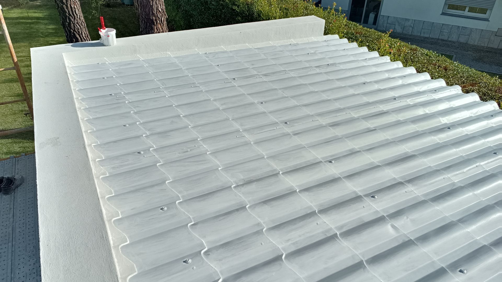 Vista de cima de um edifício com telhado de zinco branco ondulado, cercado por vegetação.