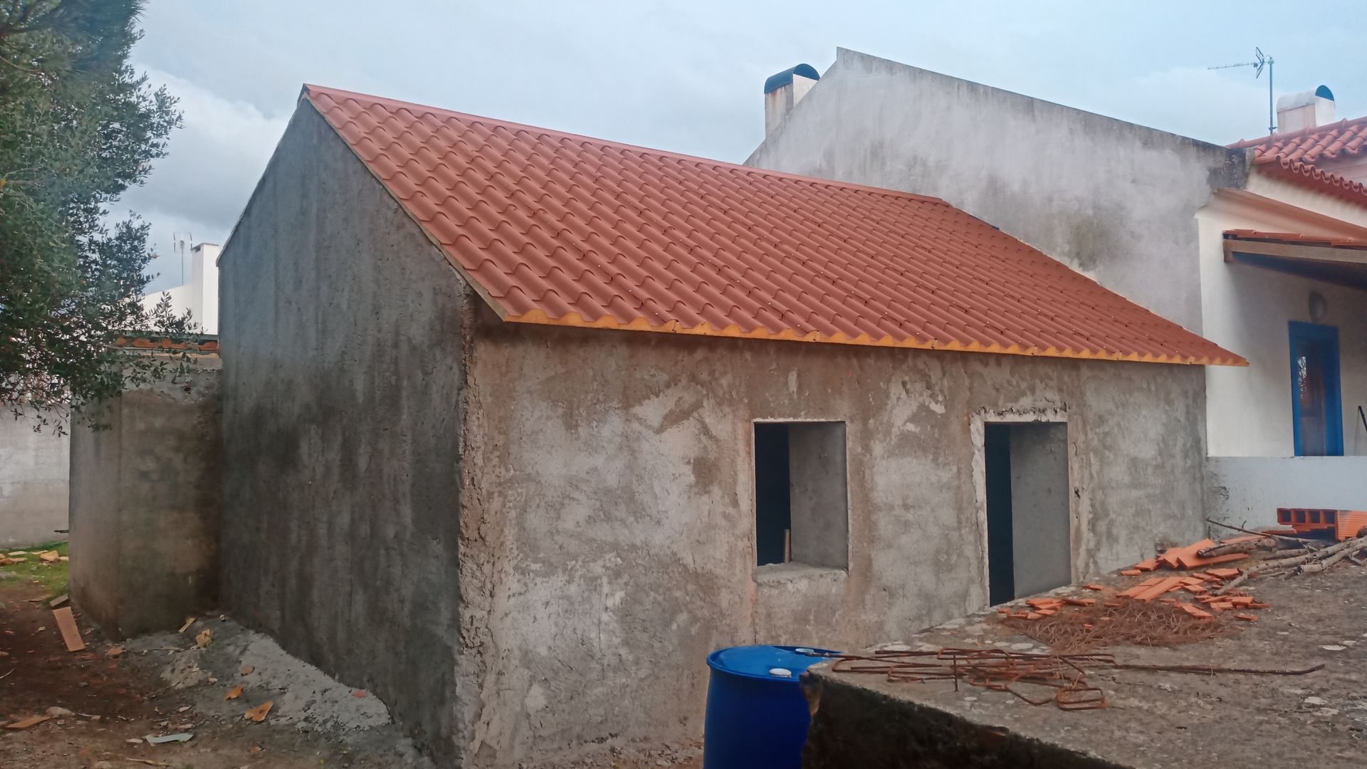 Pequeno prédio de concreto em construção com novo telhado de telhas vermelhas.