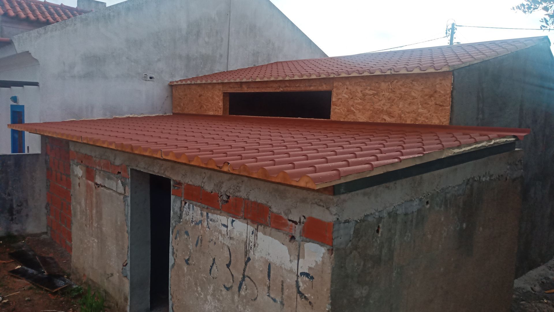 Uma pequena construção de concreto inacabada com telhado de telhas vermelhas e uma parte superior de madeira.