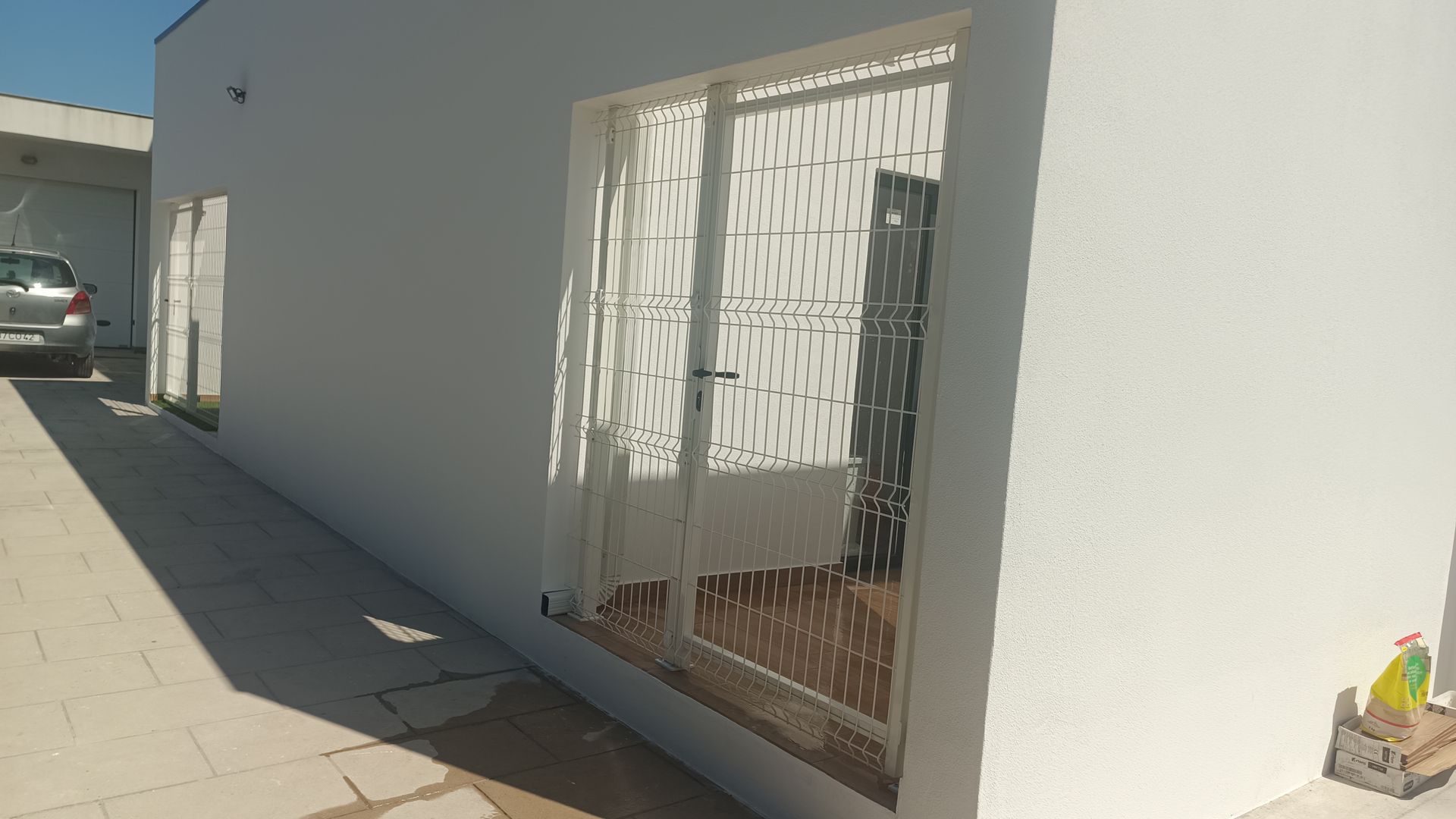 Prédio branco com janela, portão de segurança e carro na entrada.
