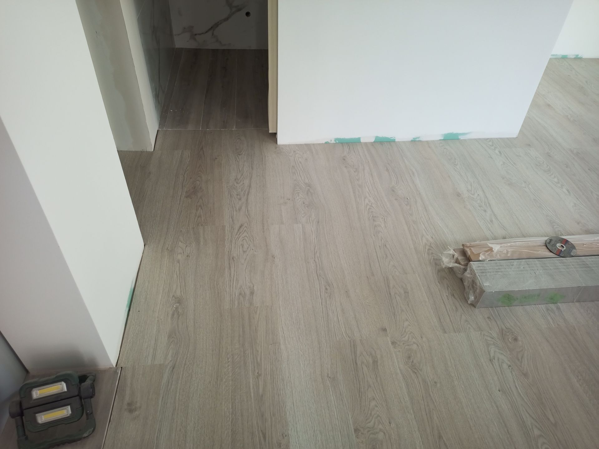 Piso recém-instalado com aparência de madeira clara em um cômodo. As paredes são brancas; materiais de construção estão próximos.