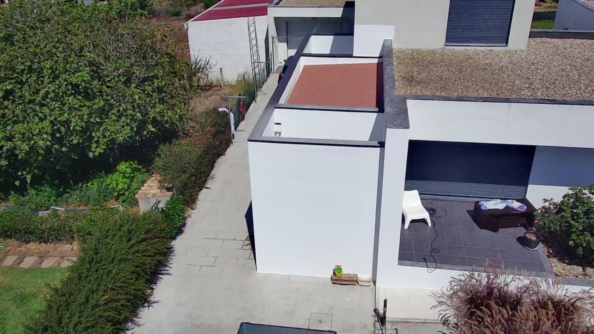 Casa moderna branca com telhado plano, rodeada de vegetação e com um pátio.