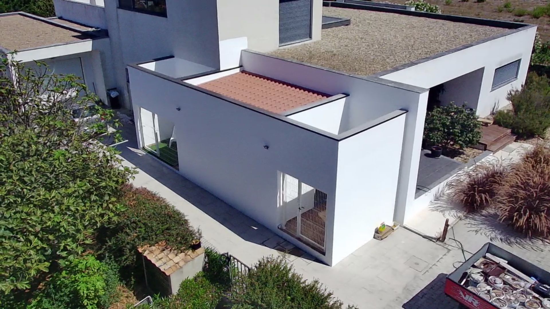 Casa moderna branca com telhados planos e um pátio aberto, rodeada de vegetação.