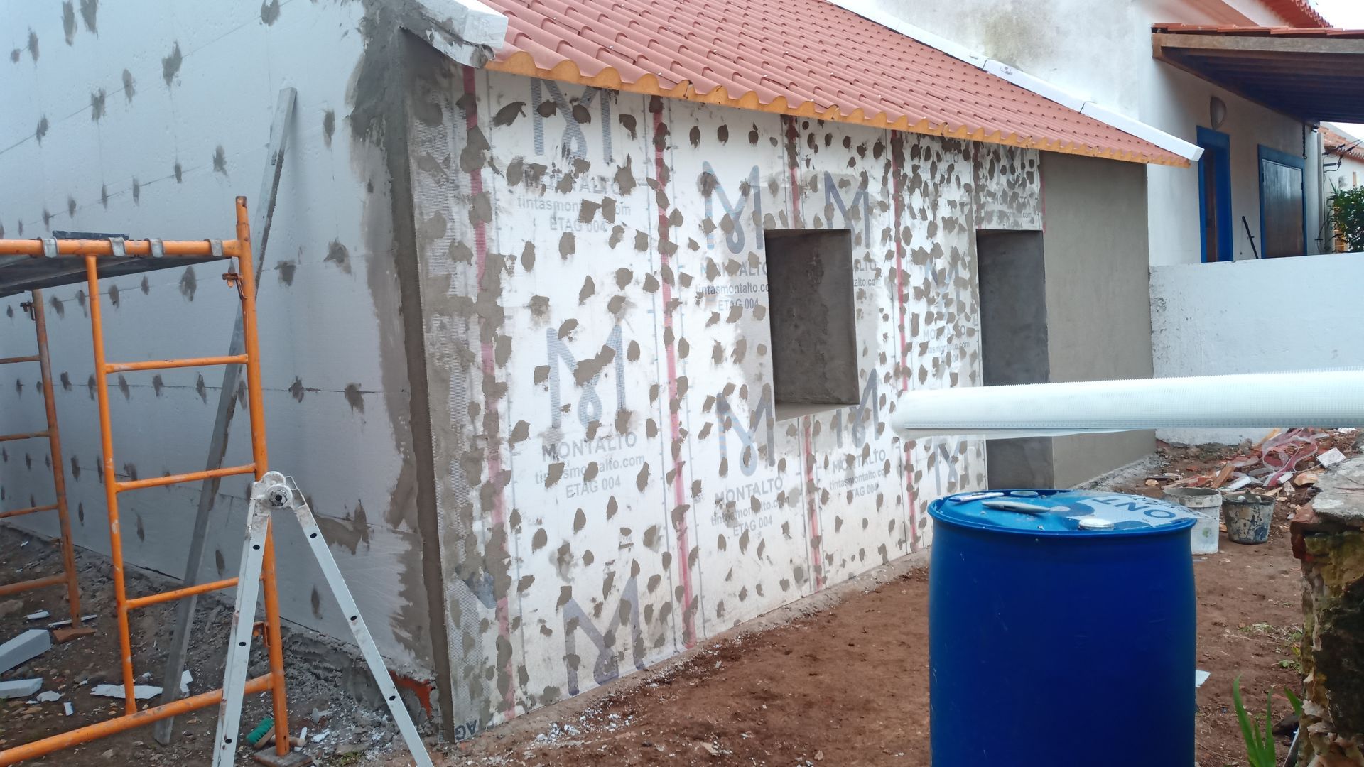 Fachada de edifício em construção com painéis de isolamento de espuma expostos e andaimes.