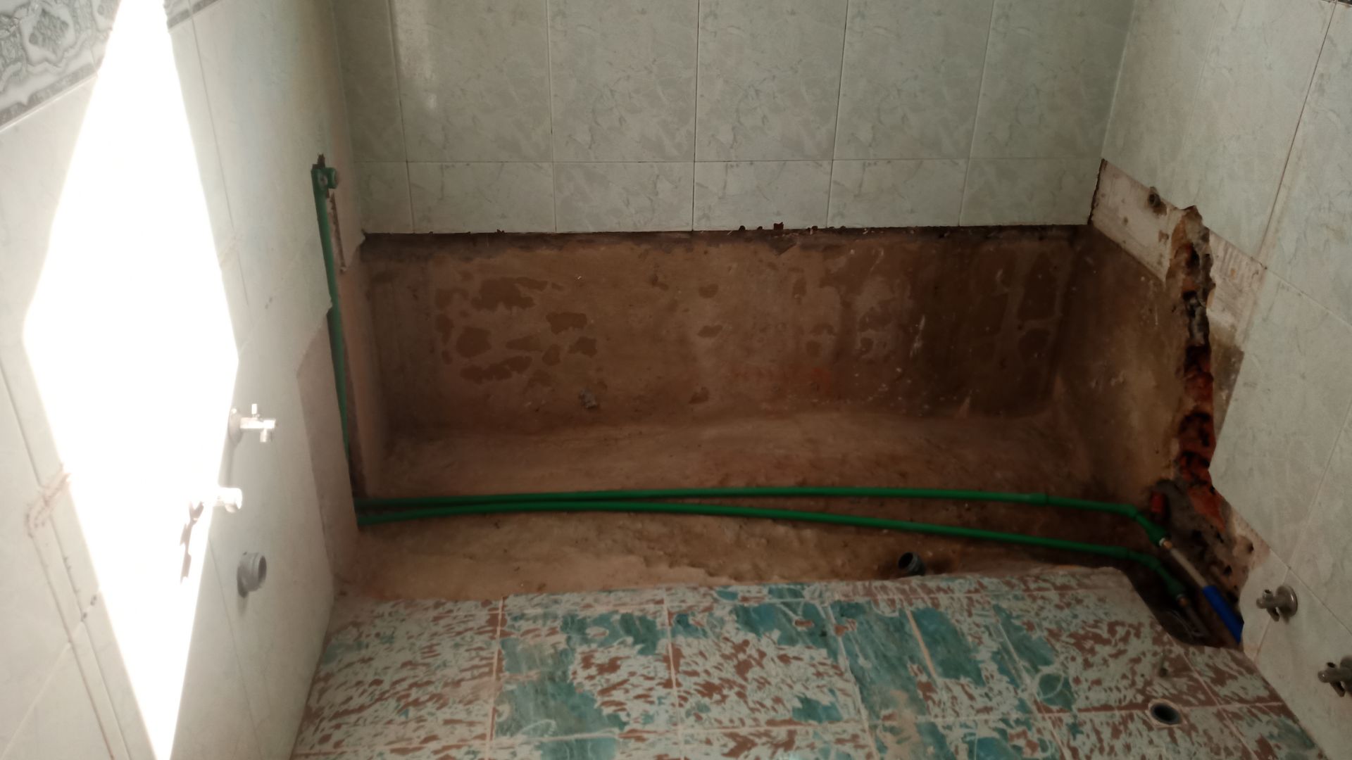 Banheiro em reforma; canos verdes em contraste com uma parede marrom aparente. Paredes revestidas com azulejos.