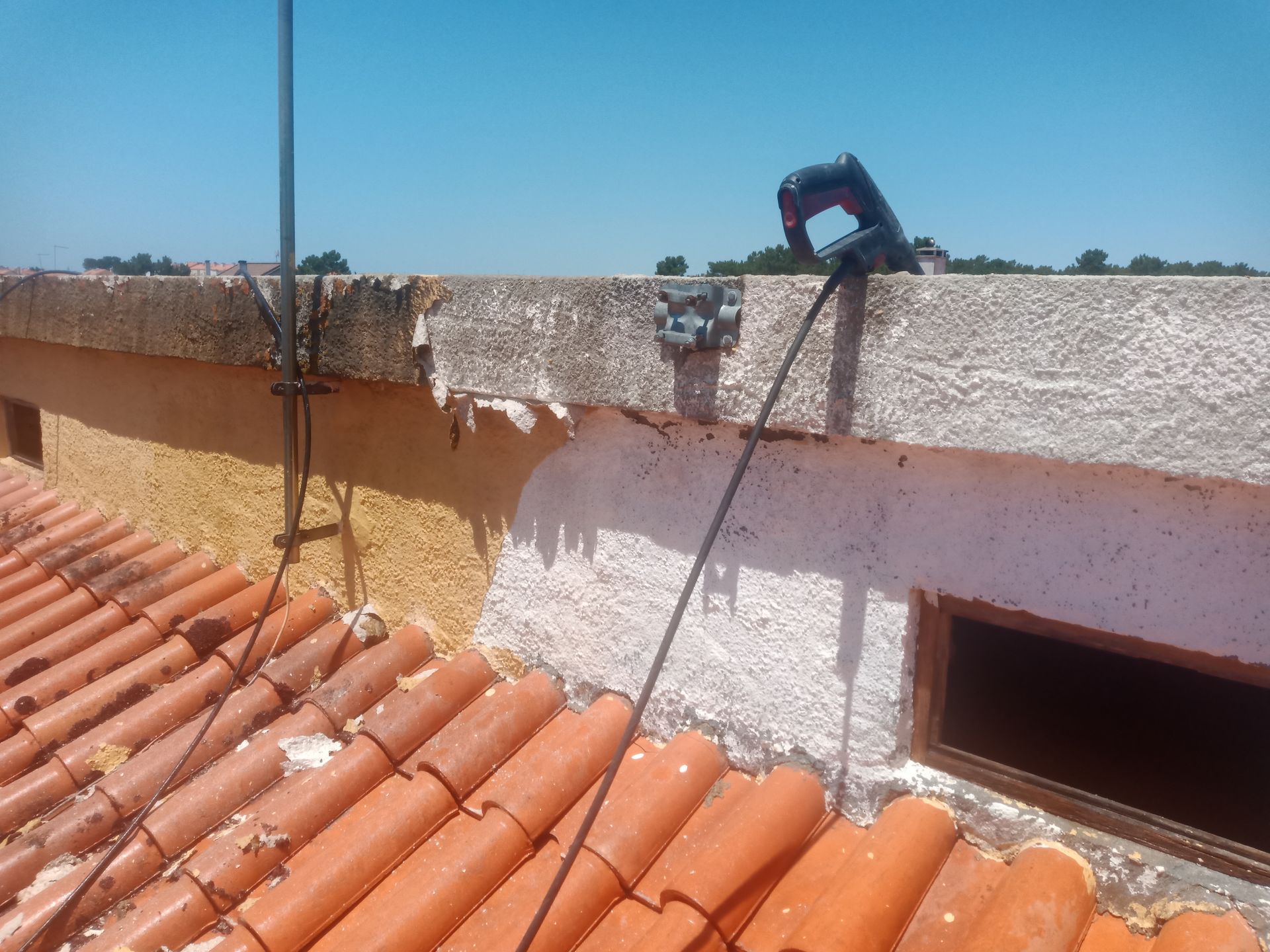 Vista do telhado de um prédio com telhas vermelhas, borda danificada e uma serra recíproca.