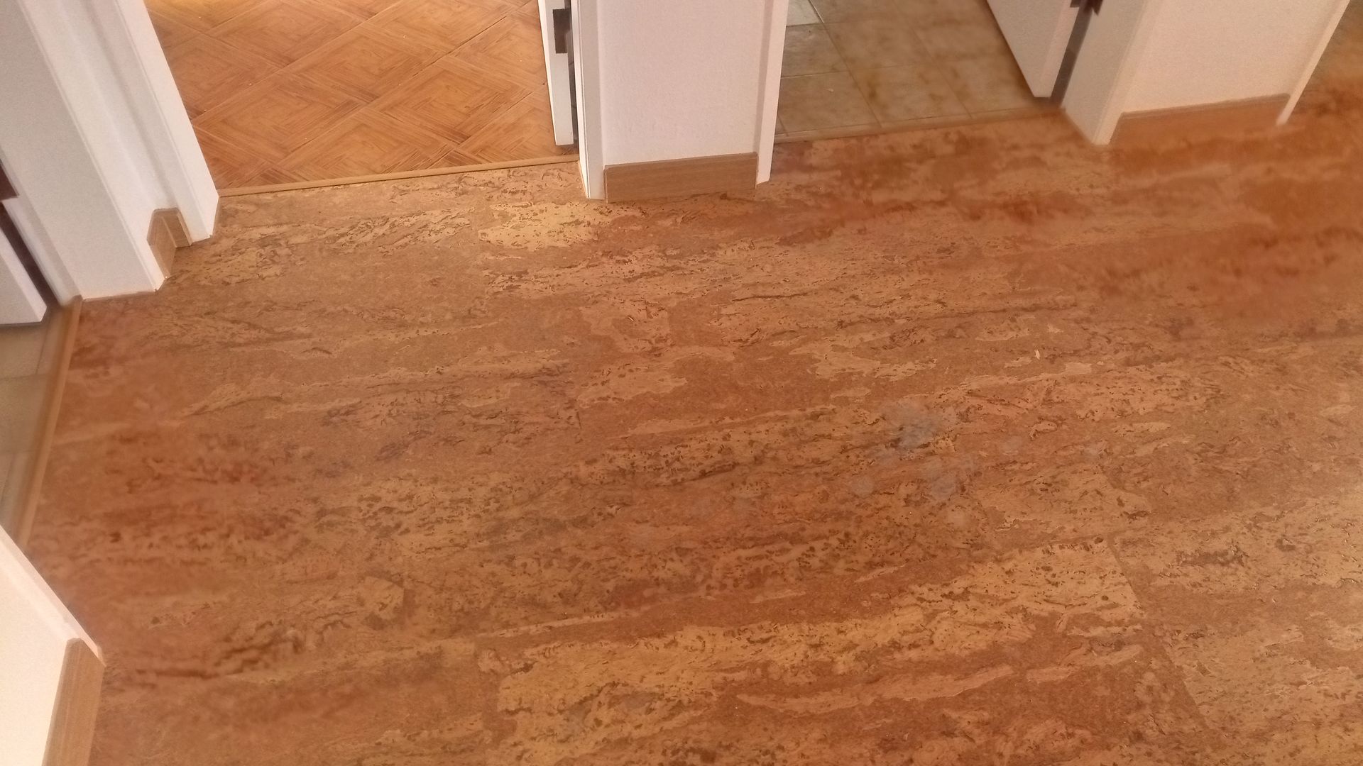 Piso de pedra marrom com manchas e batentes de portas visíveis.
