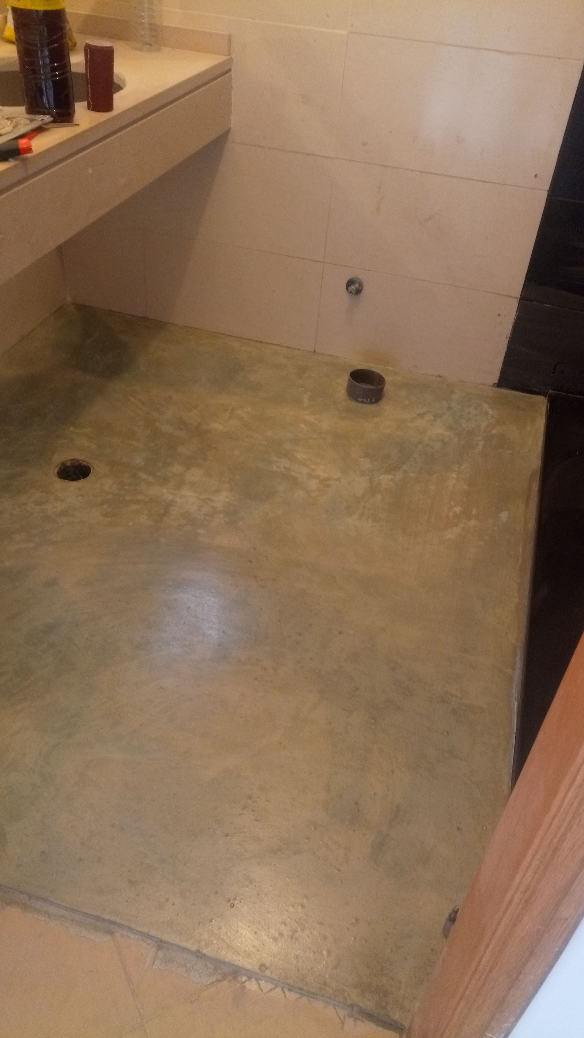 Piso do banheiro com dois ralos e parede de concreto na cor dourada.