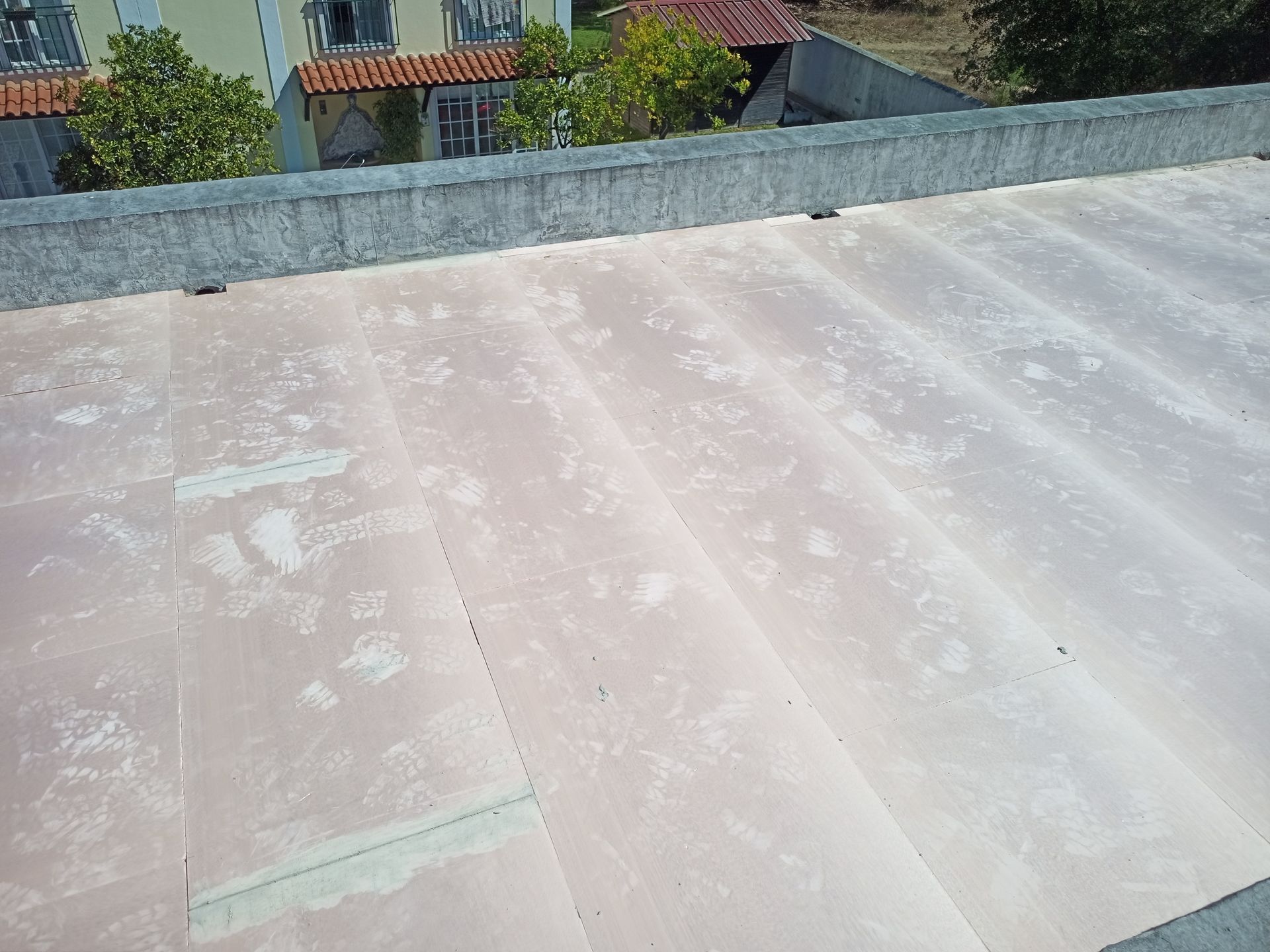 Telhado branco-rosado com detalhes em concreto e pequenos objetos escuros, visto de cima, provavelmente pertencente a um edifício.