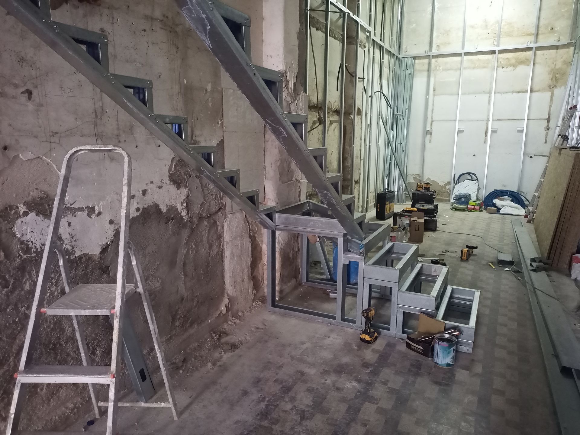 Canteiro de obras: escada metálica em construção ao lado de uma parede parcialmente demolida; escada de mão à esquerda.