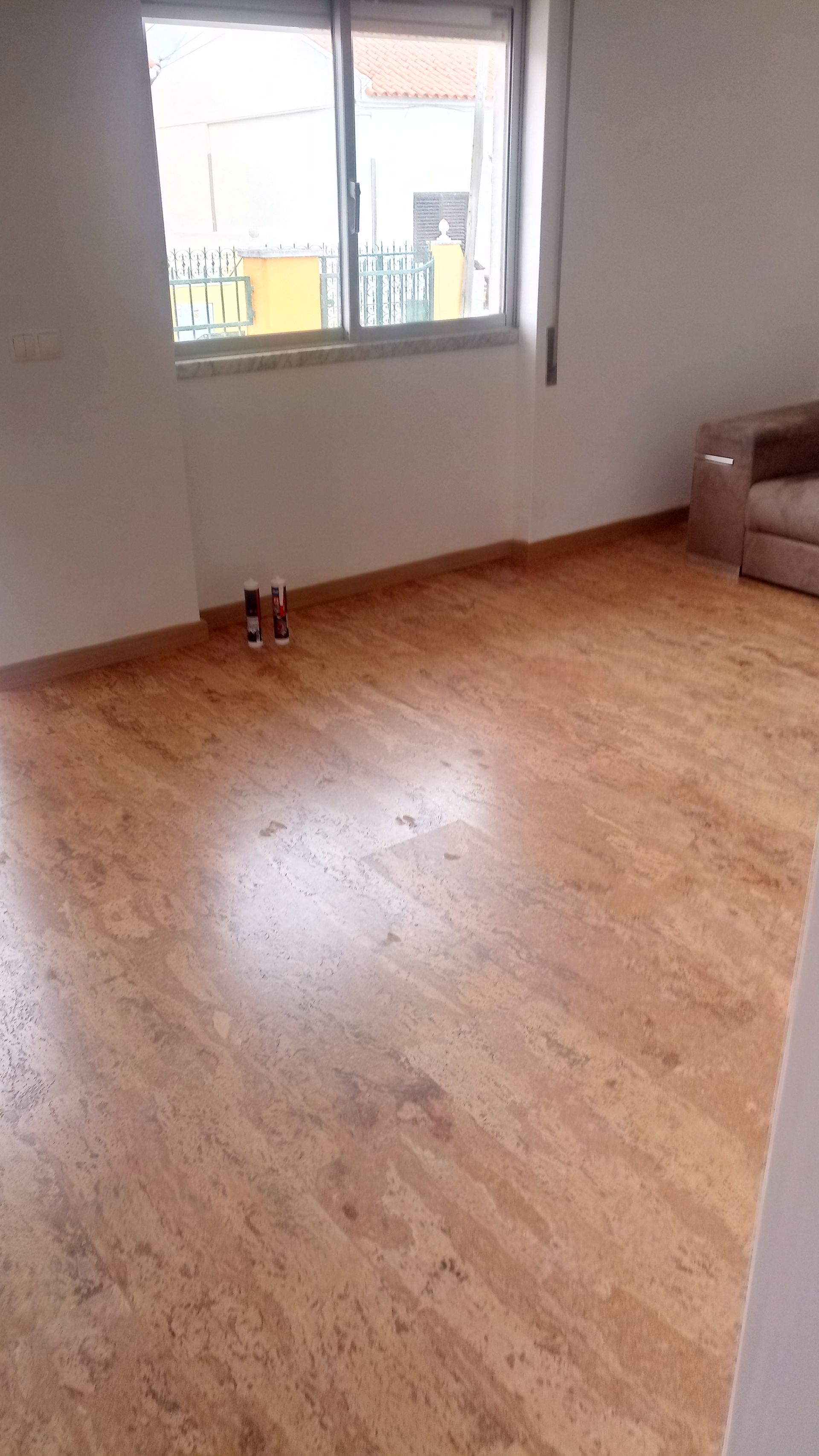 Quarto vazio com piso de cortiça, uma janela e uma poltrona bege.