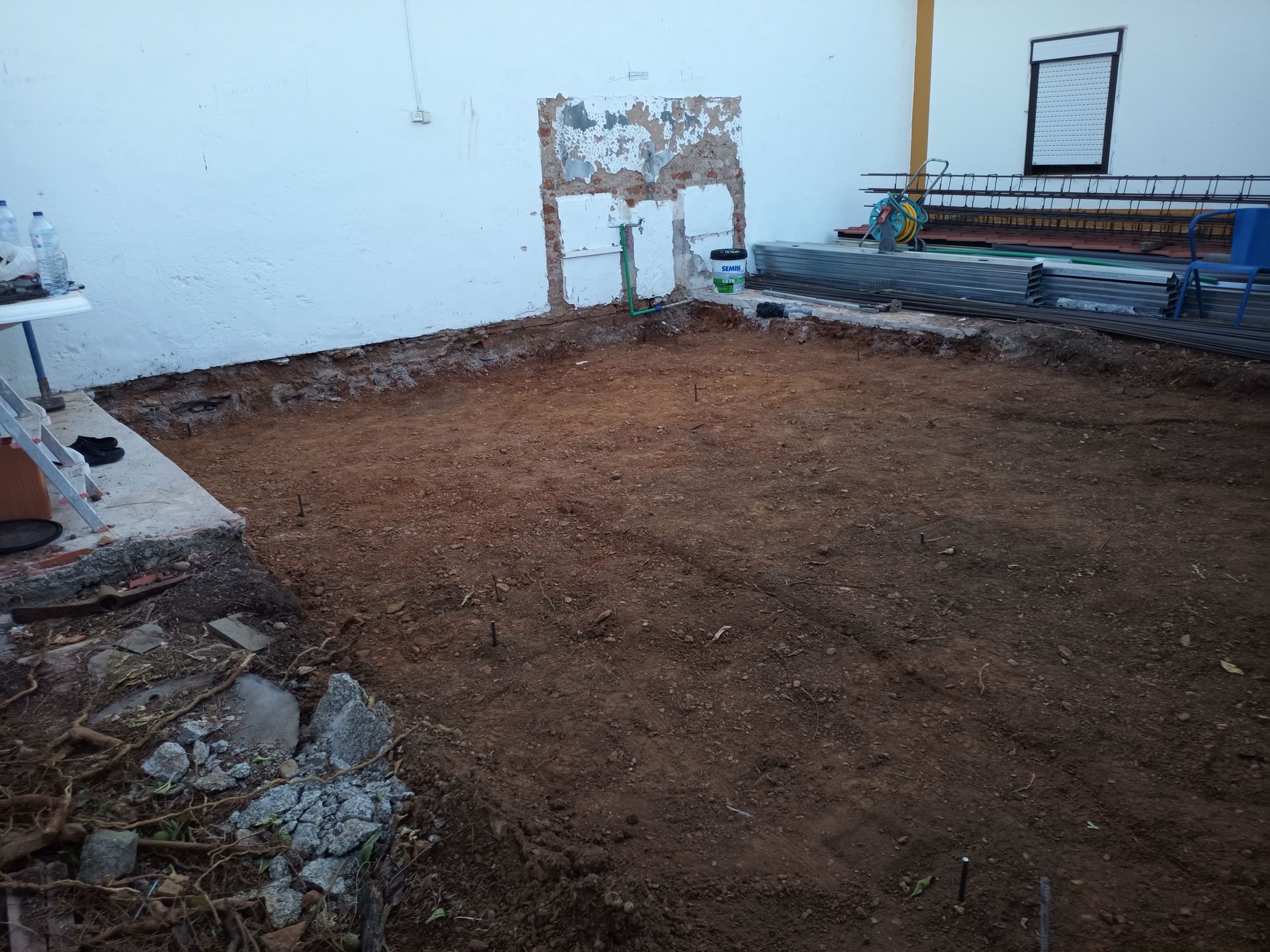 Piso de terra batida com um recorte retangular na parede, possivelmente uma antiga porta. Prédio branco.