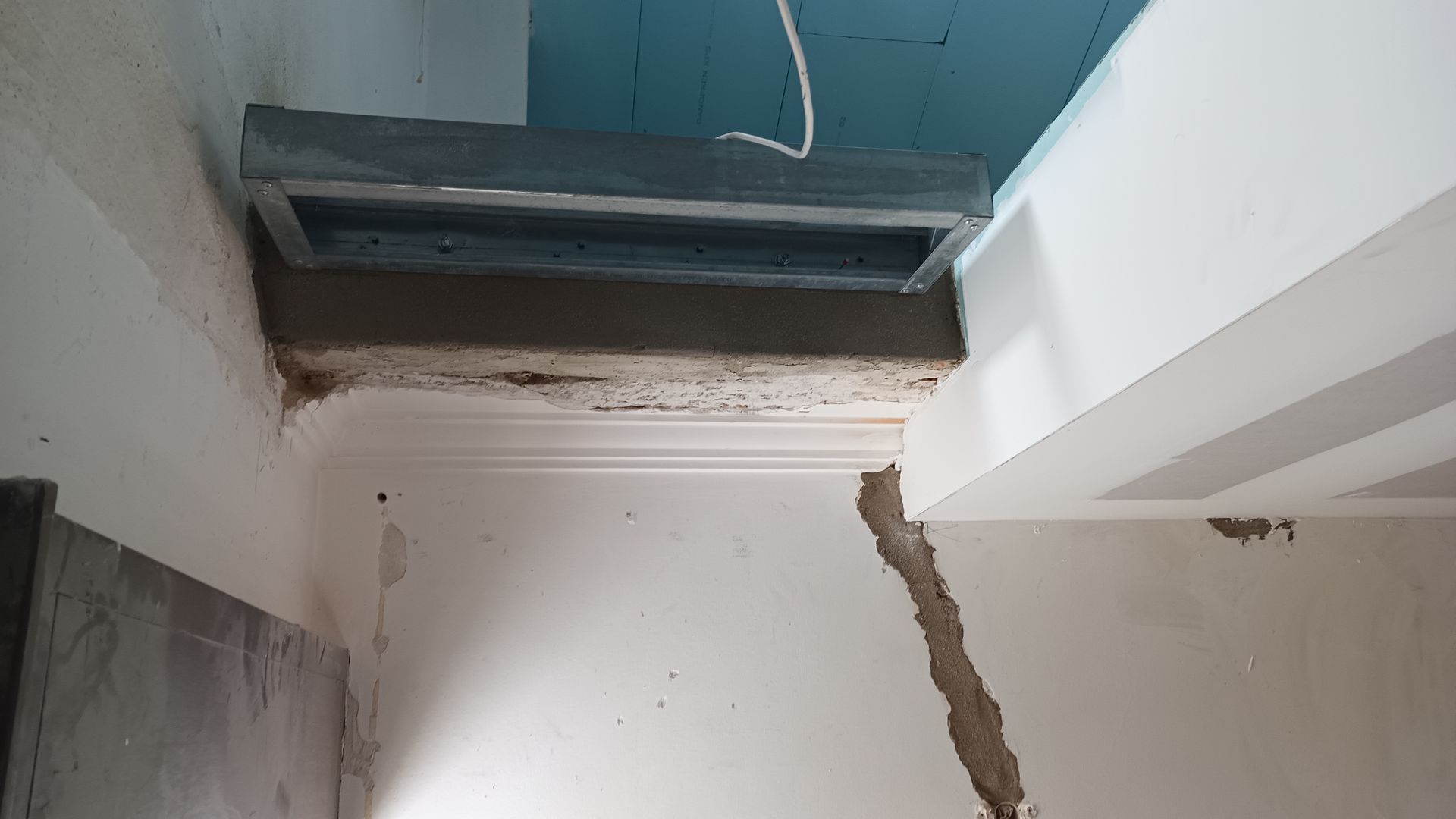 Interior com construção inacabada: ventilação no teto, parede danificada e estrutura exposta.