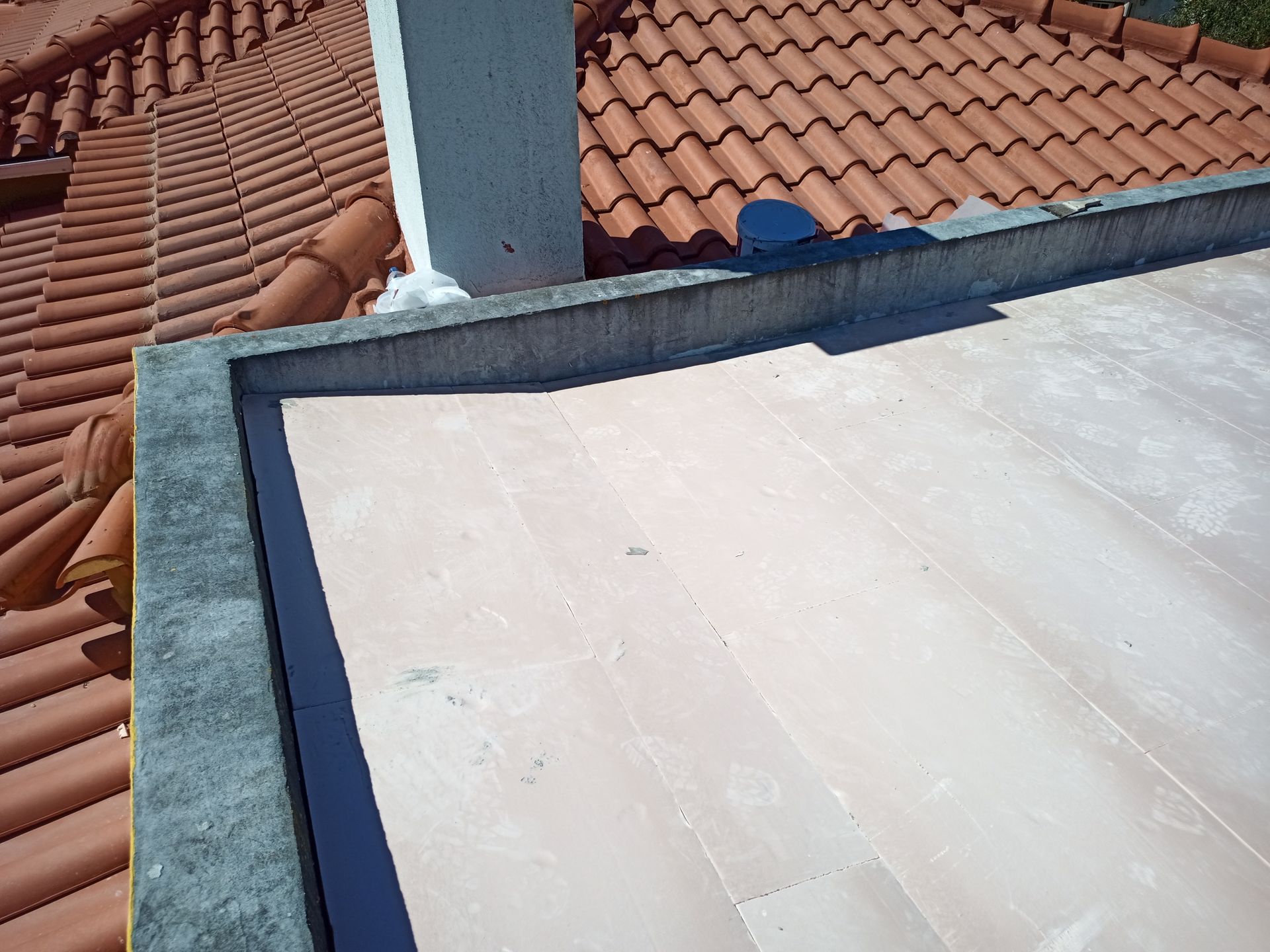 Telhado plano ao lado de um telhado de telhas, com borda de concreto.