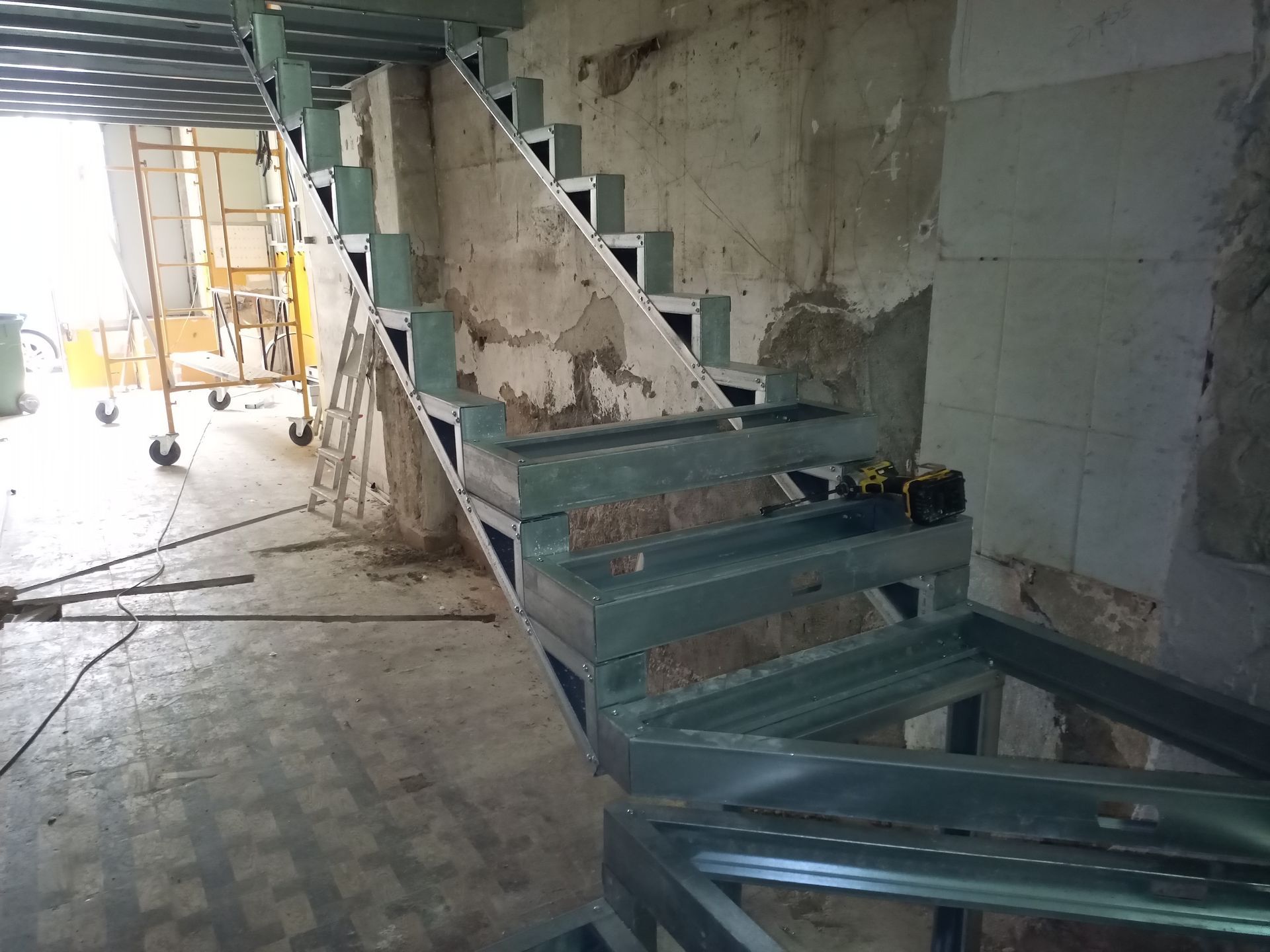 Estrutura metálica de escada em construção dentro de um edifício com paredes deterioradas.