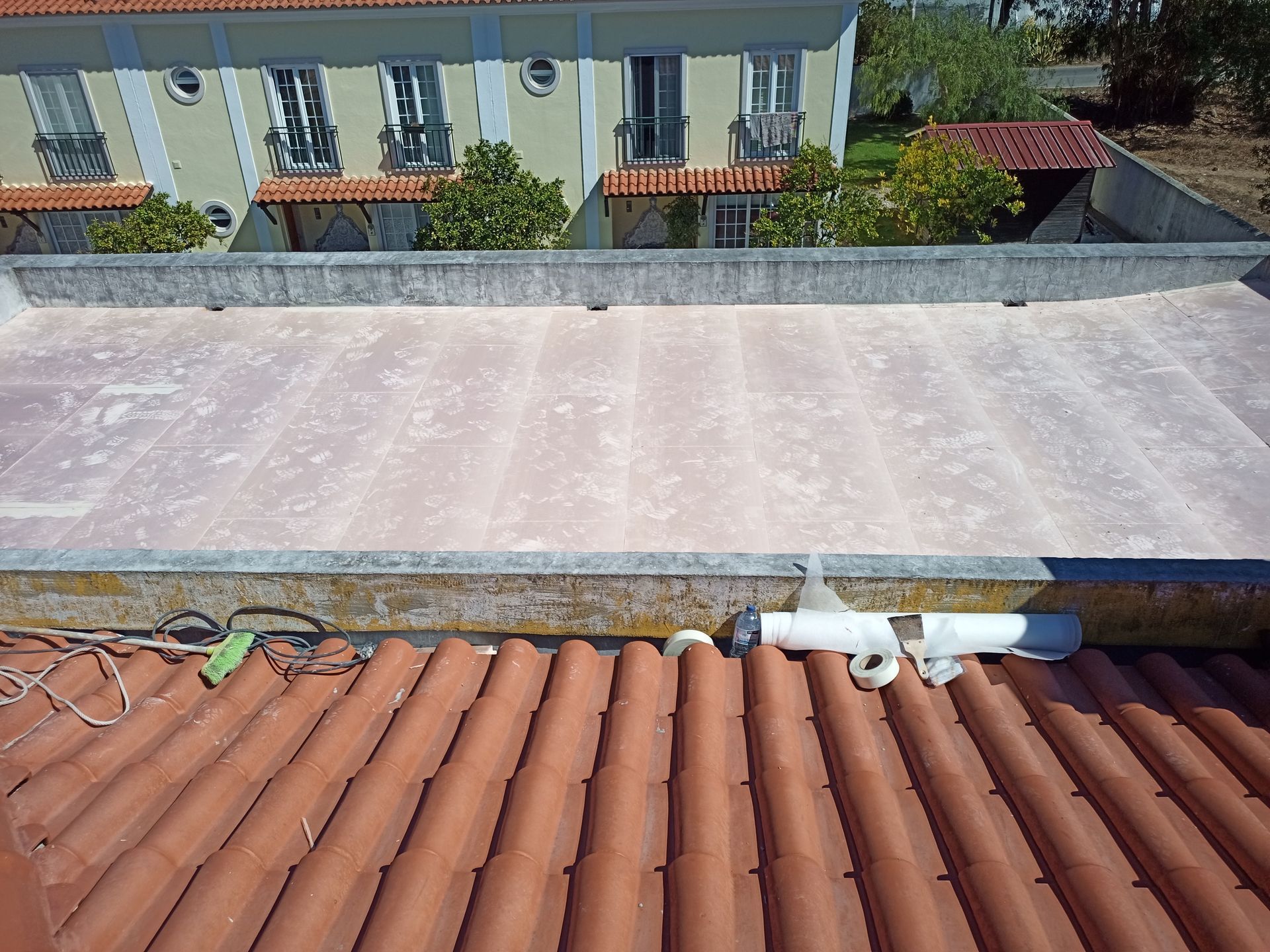 Vista de dois telhados: telhado de telha vermelha em primeiro plano, telhado plano e desgastado ao fundo com um edifício.