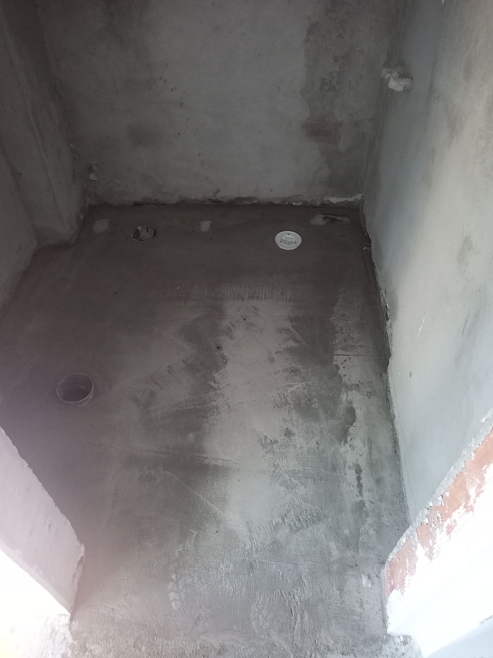 Sala com paredes de concreto em construção; piso de concreto aparente com furos para canos.