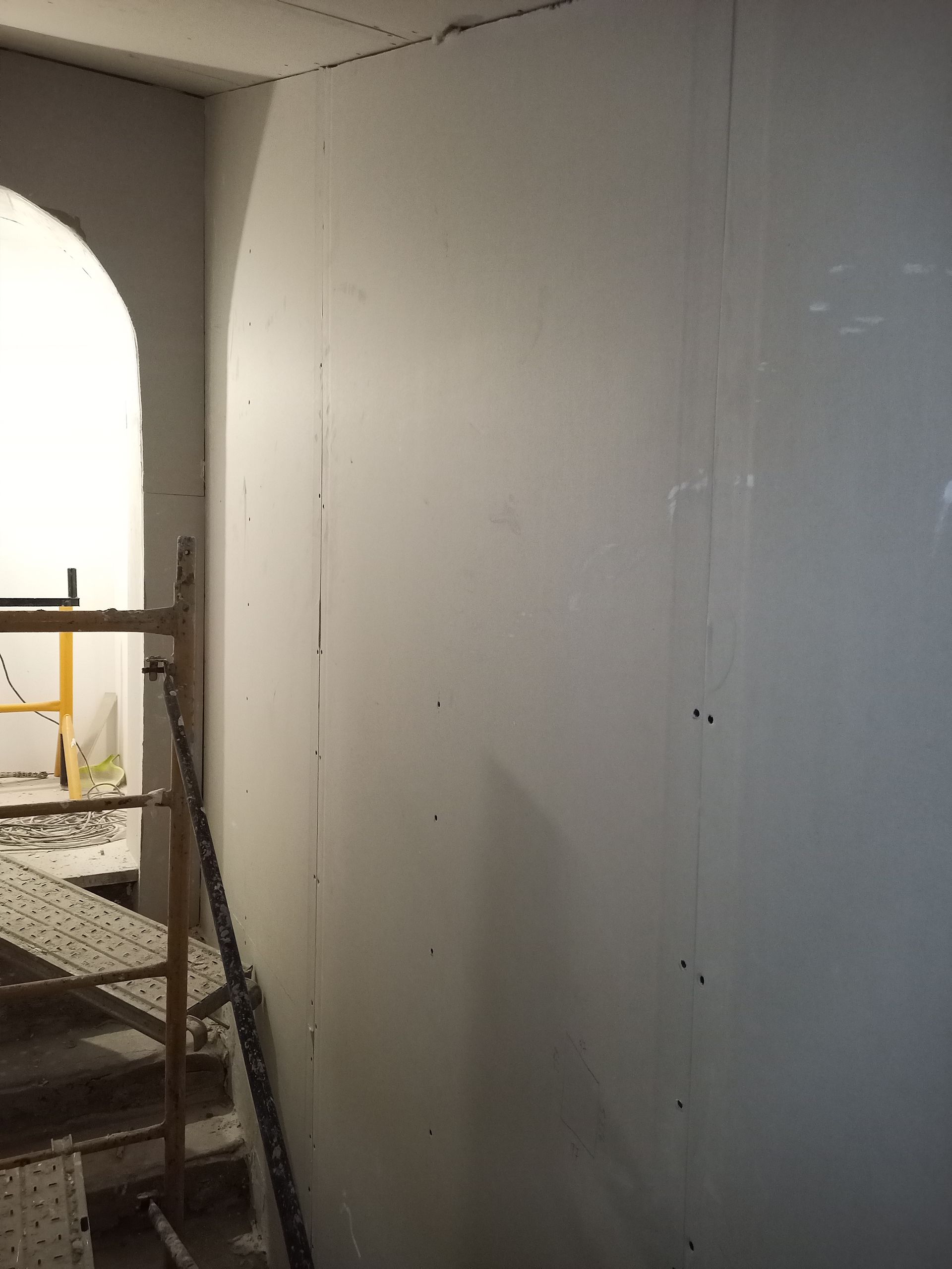 Cena de construção: paredes brancas, andaimes, porta em arco.