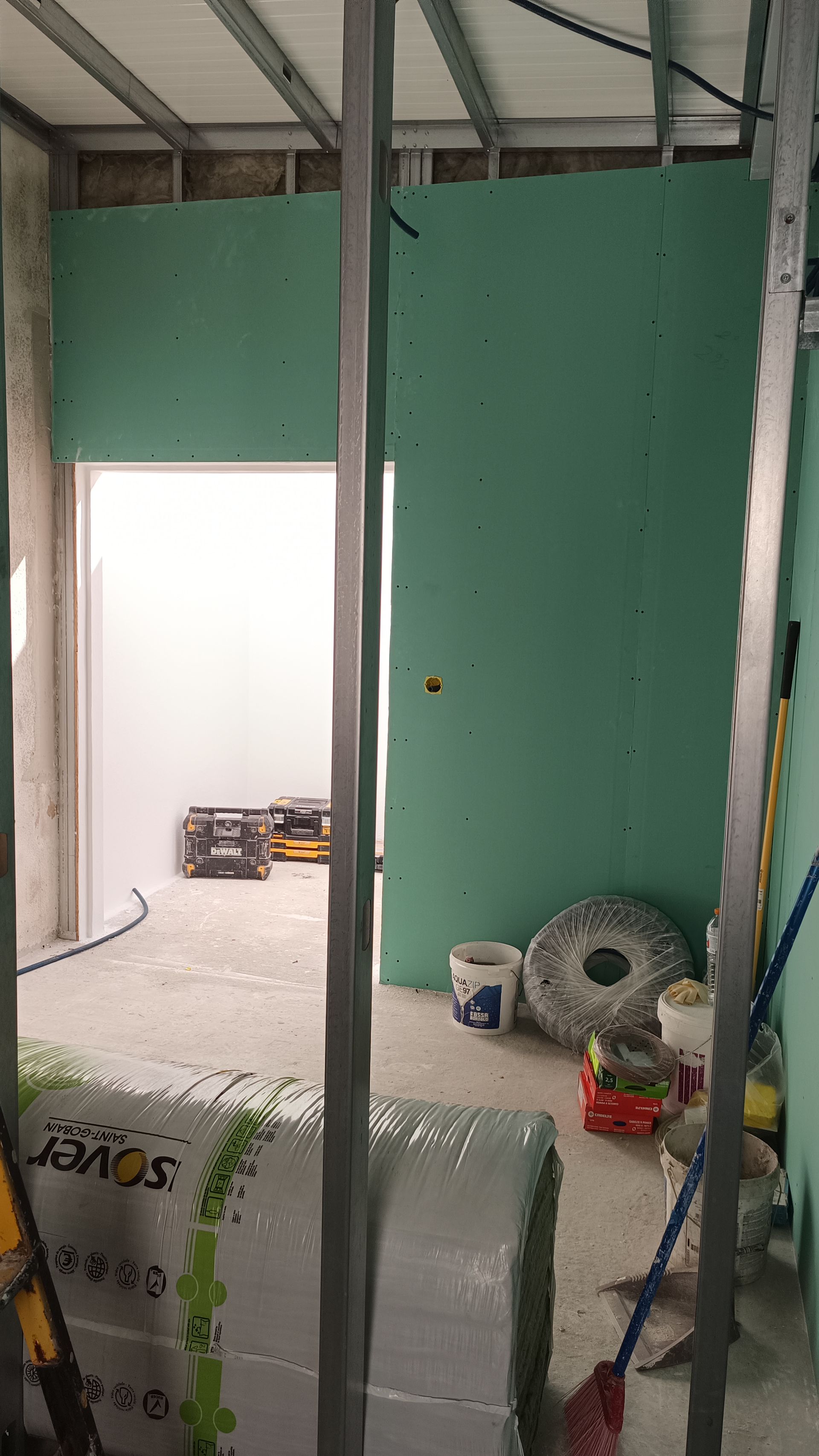 Interior de um cômodo em construção com drywall verde, estrutura metálica e materiais de construção.