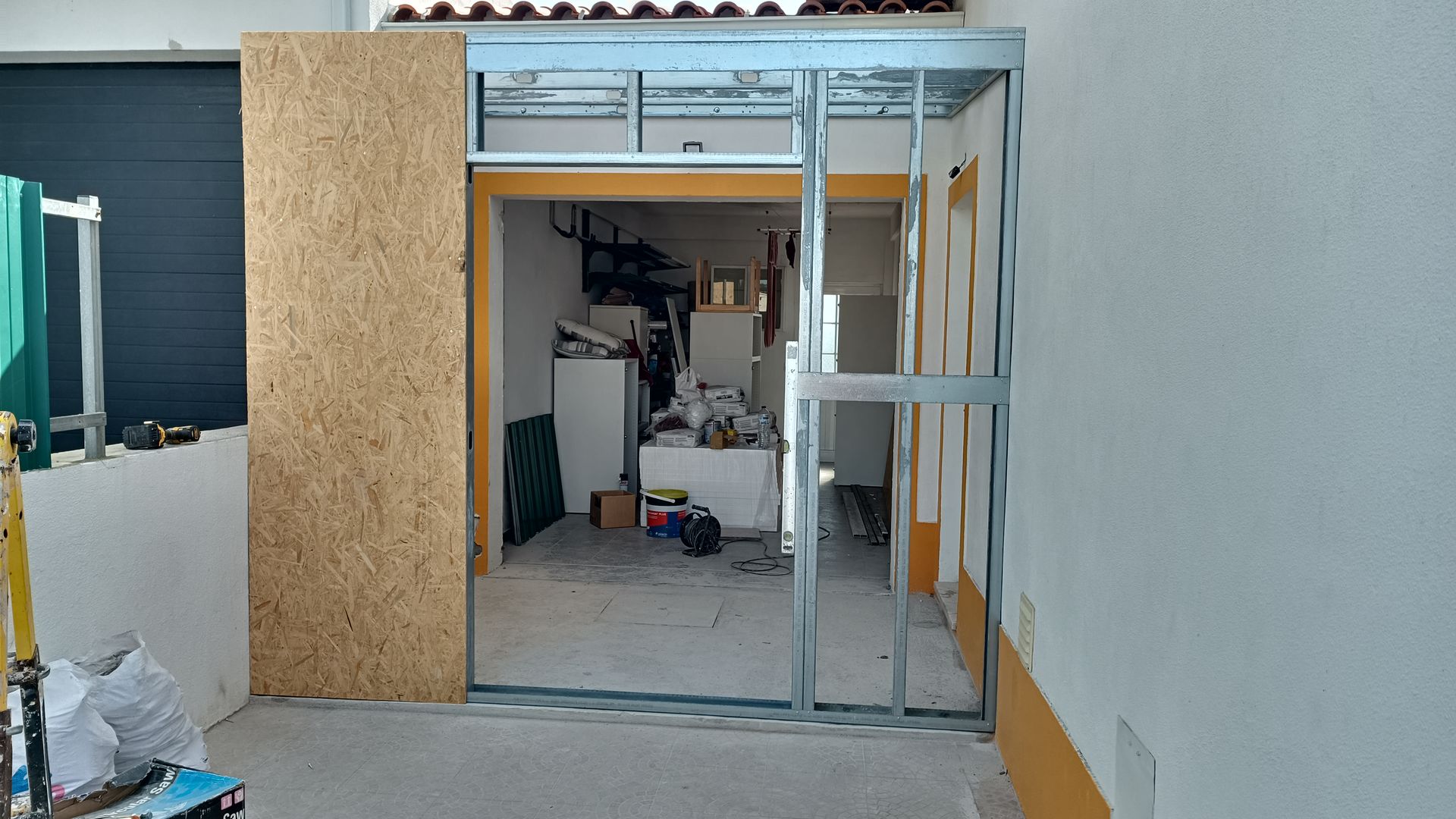 Construção da porta com estrutura metálica. Paredes parcialmente revestidas em um espaço semelhante a uma garagem, com algumas áreas em OSB expostas.