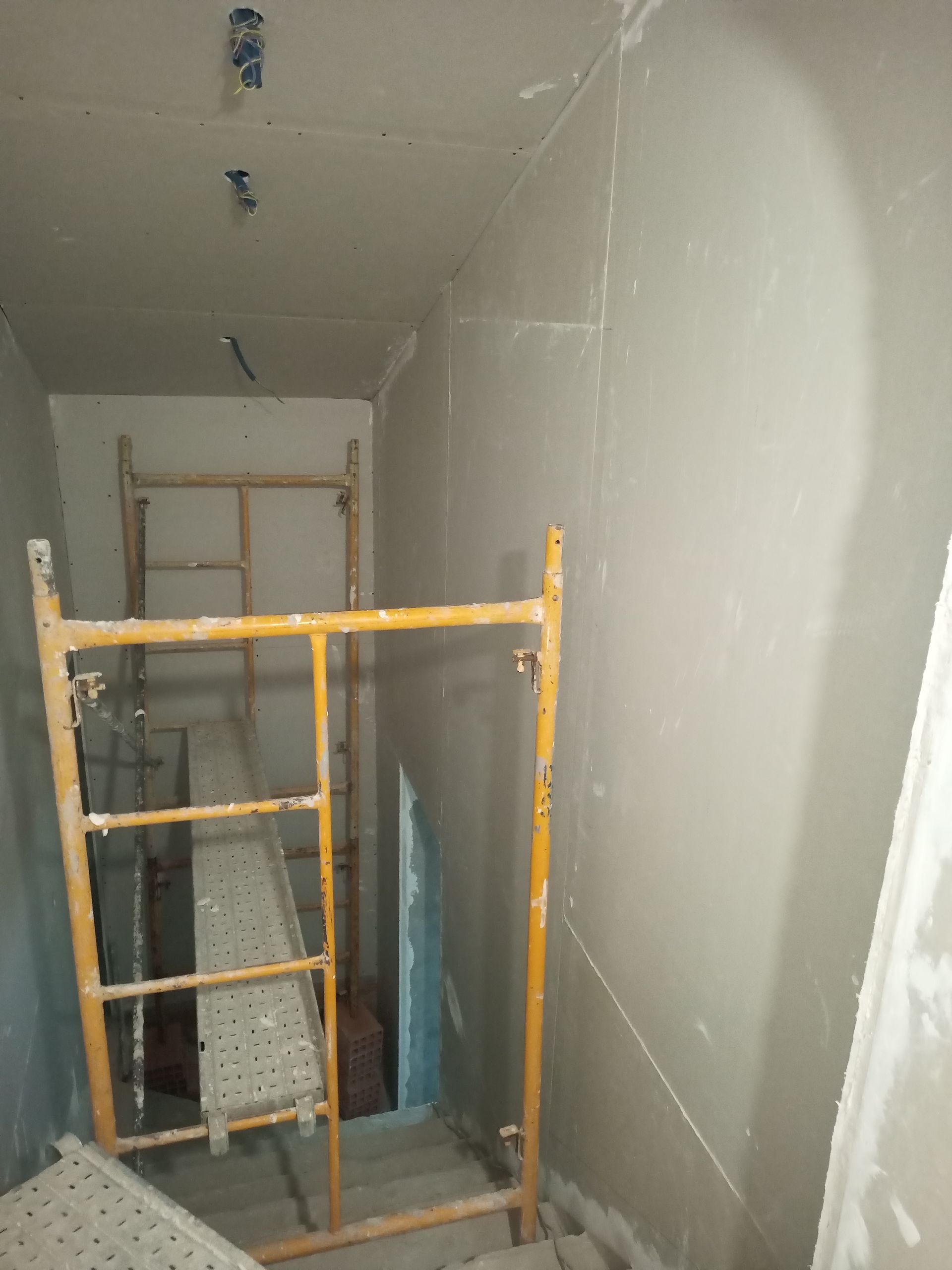 Construção em uma escadaria: drywall, andaimes, paredes inacabadas e teto.