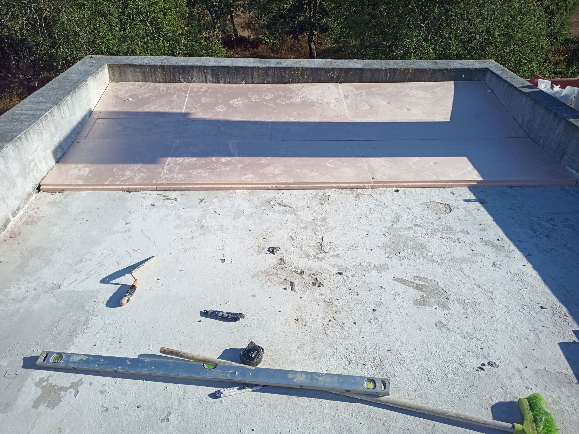 Telhado de concreto com uma seção de placas de isolamento rosa e ferramentas espalhadas.