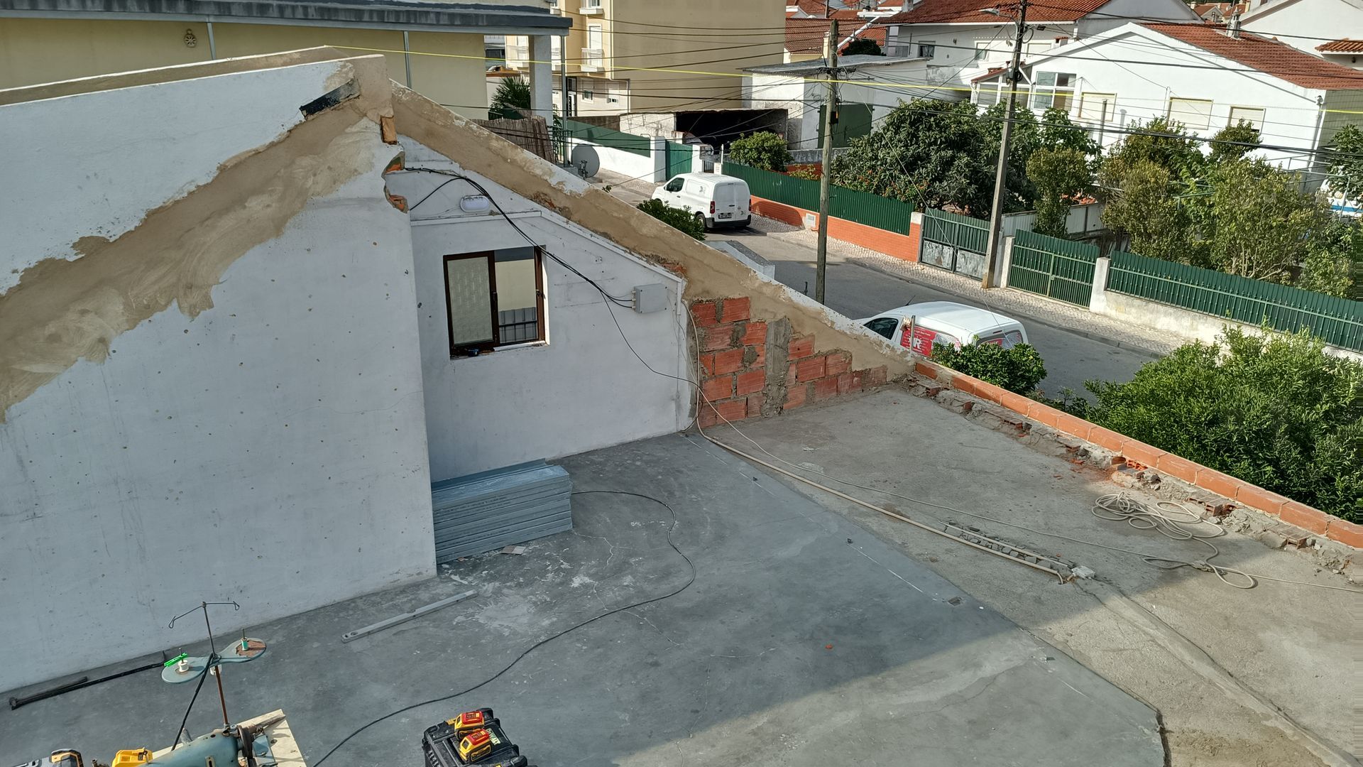 Vista do telhado de um prédio branco e da rua com uma van branca estacionada. Telhado de concreto e paredes de tijolo.