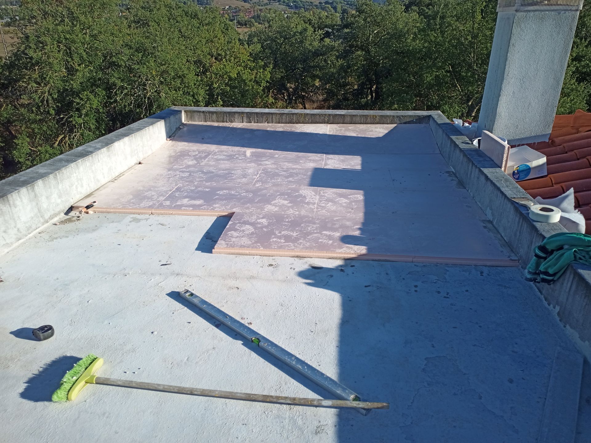 Telhado plano de concreto com revestimento rosa, ferramentas próximas e uma chaminé.