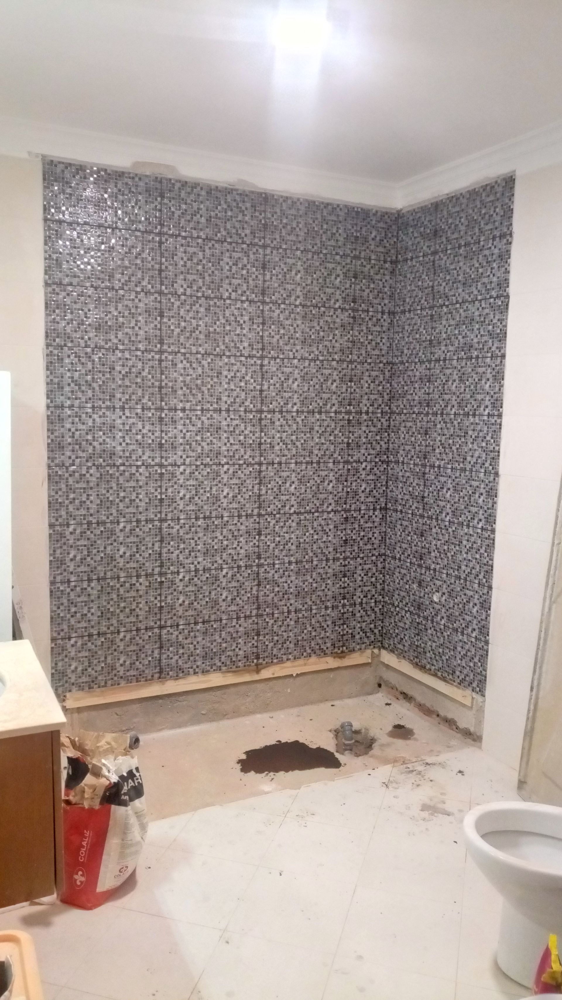 Banheiro em construção, paredes com azulejos em mosaico. Argamassa seca no piso.