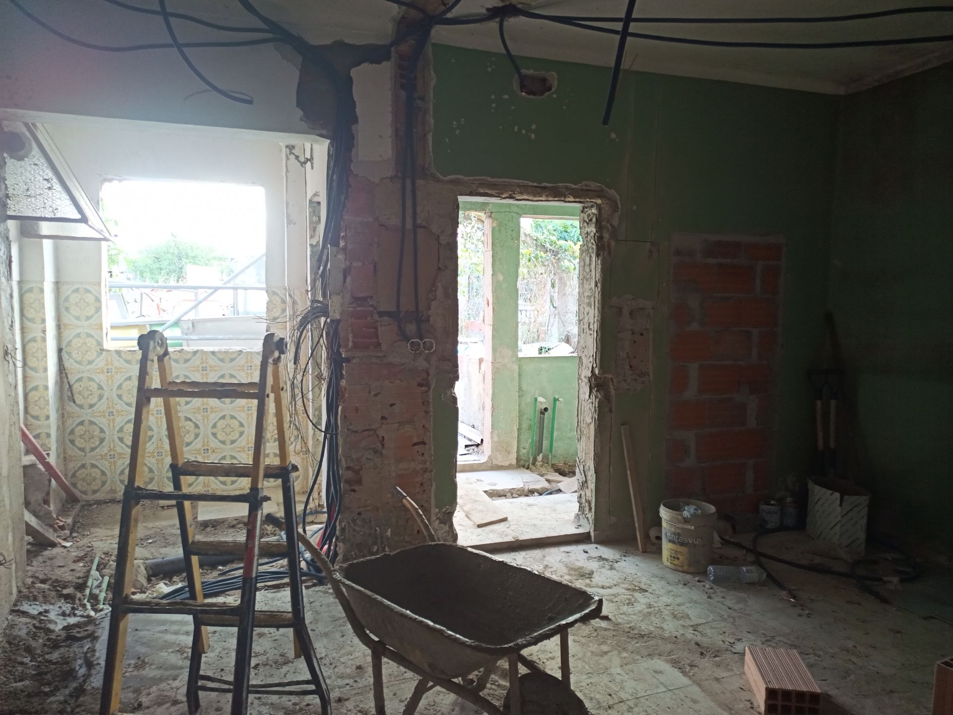 Quarto em reforma com fiação exposta, escada, carrinho de mão e alvenaria.