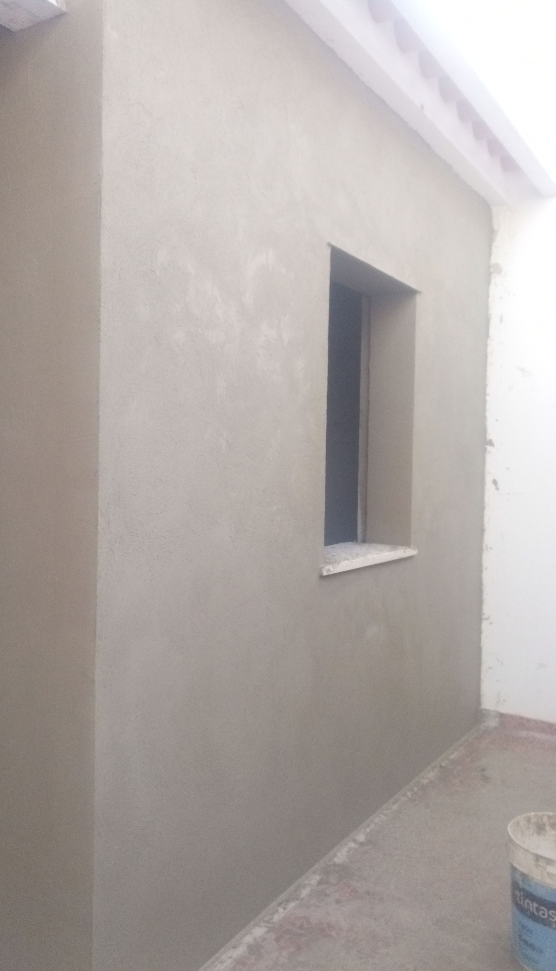 Parede externa com janela quadrada, revestida com estuque cinza-claro.