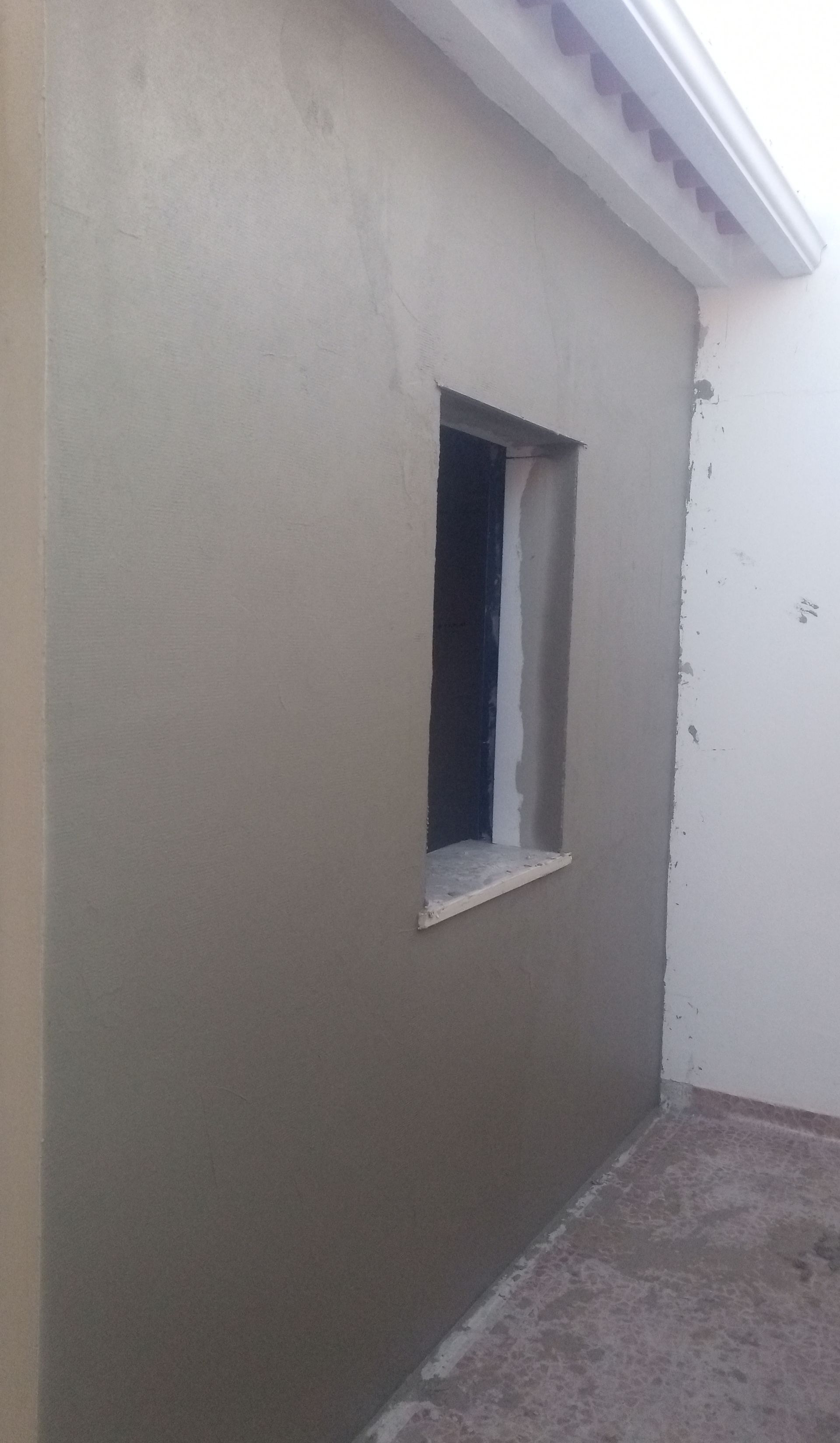 Parede externa com janela, recém-rebocada em tom cinza claro.