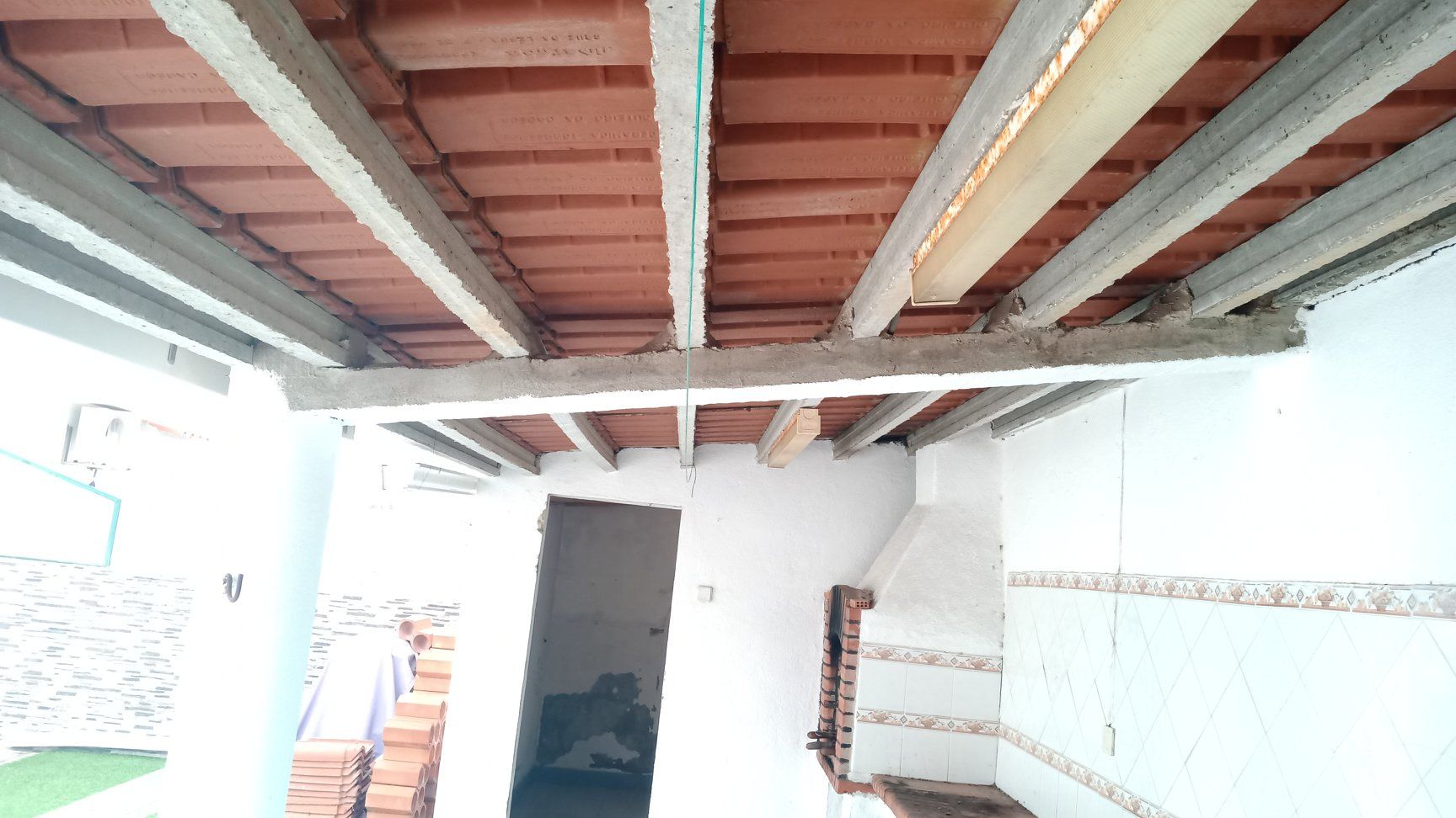 Vista do teto inacabado de uma estrutura externa com vigas expostas, ladrilhos de tijolo e uma lareira.