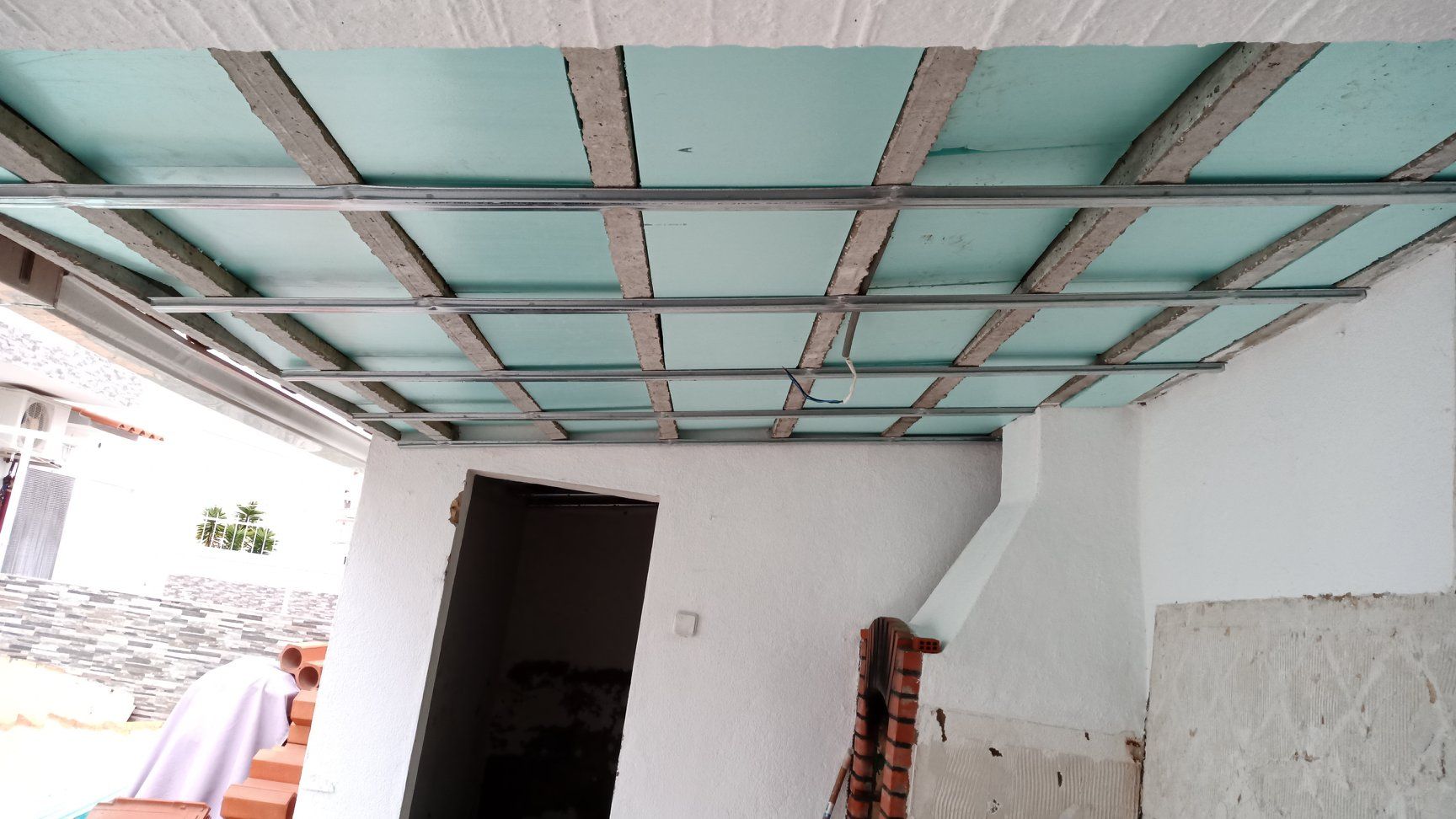 Teto em construção: estrutura metálica com painéis isolantes, próximo a uma porta e parede branca.