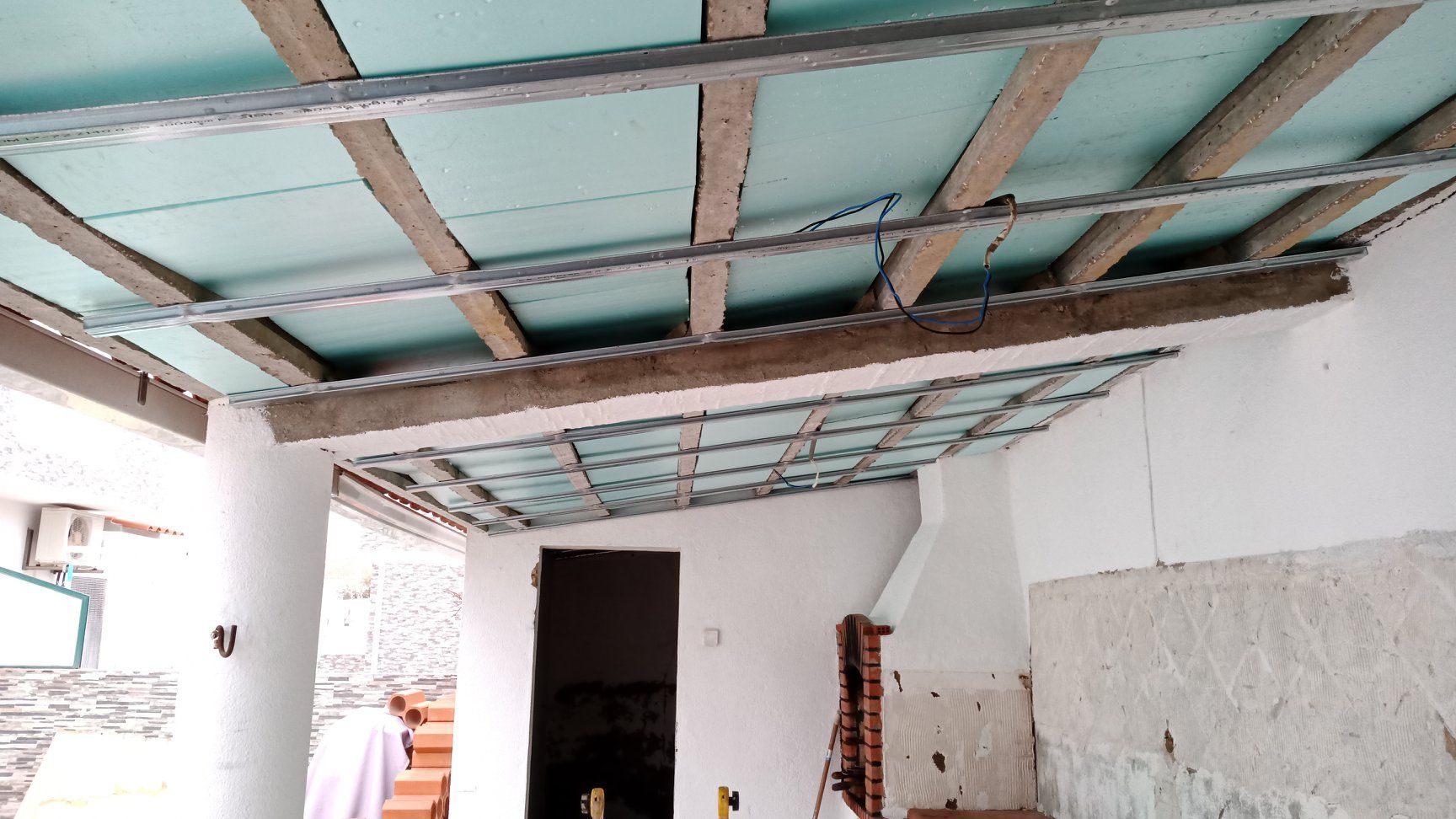 Construção de teto com vigas expostas, placas de isolamento e estrutura metálica em área externa.